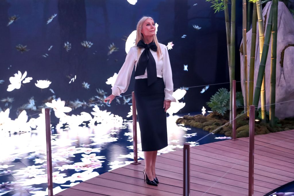 Gwyneth Paltrow standing on a wooden walkway with a water feature behind her.