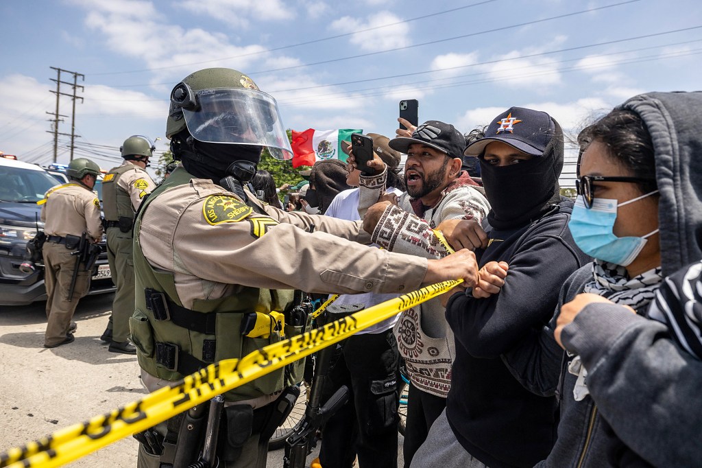 A sheriff's deputies holds backed masked protesters during a daytime riot in Paramount, Calif.