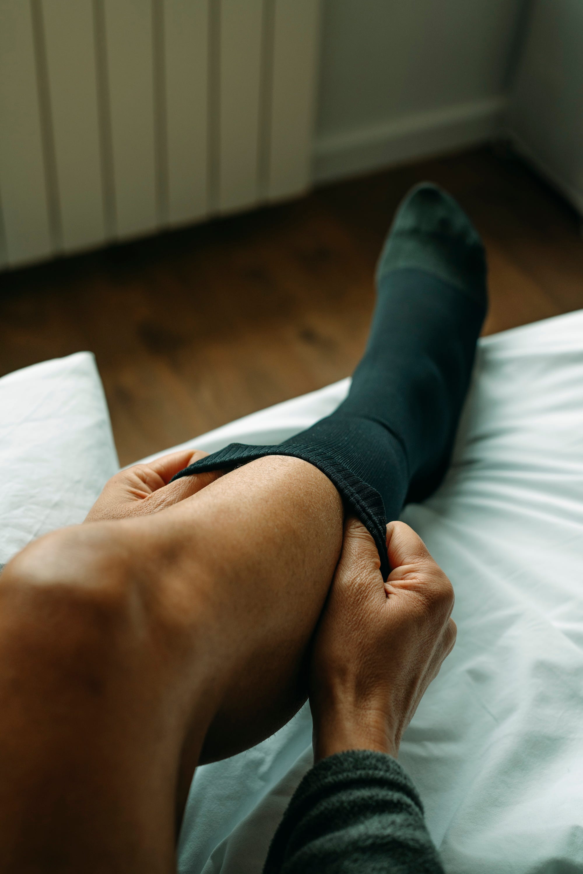 A man puts on black compression socks on a bed.