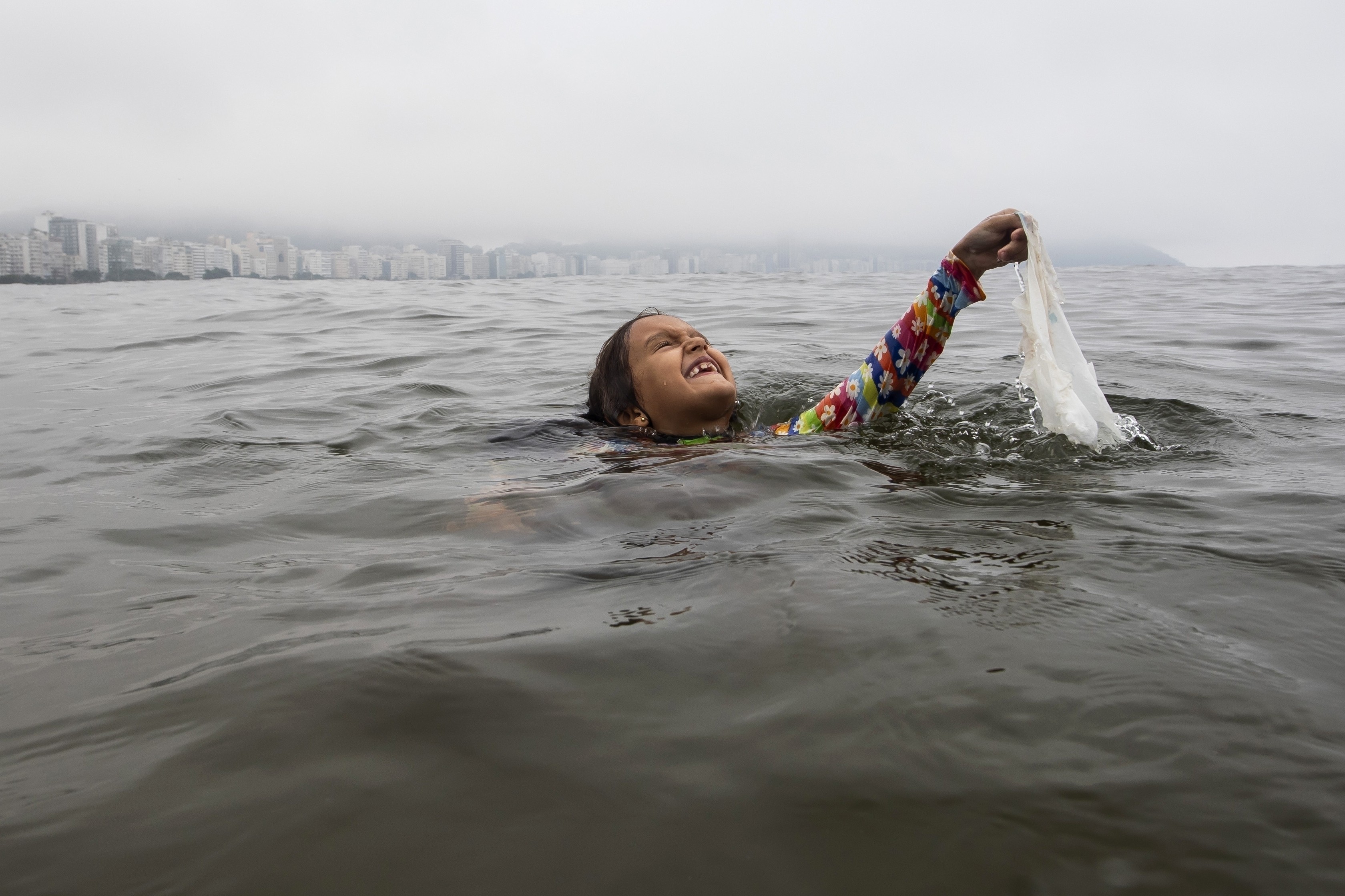 A young person lifts a plastic bag up while swimming.