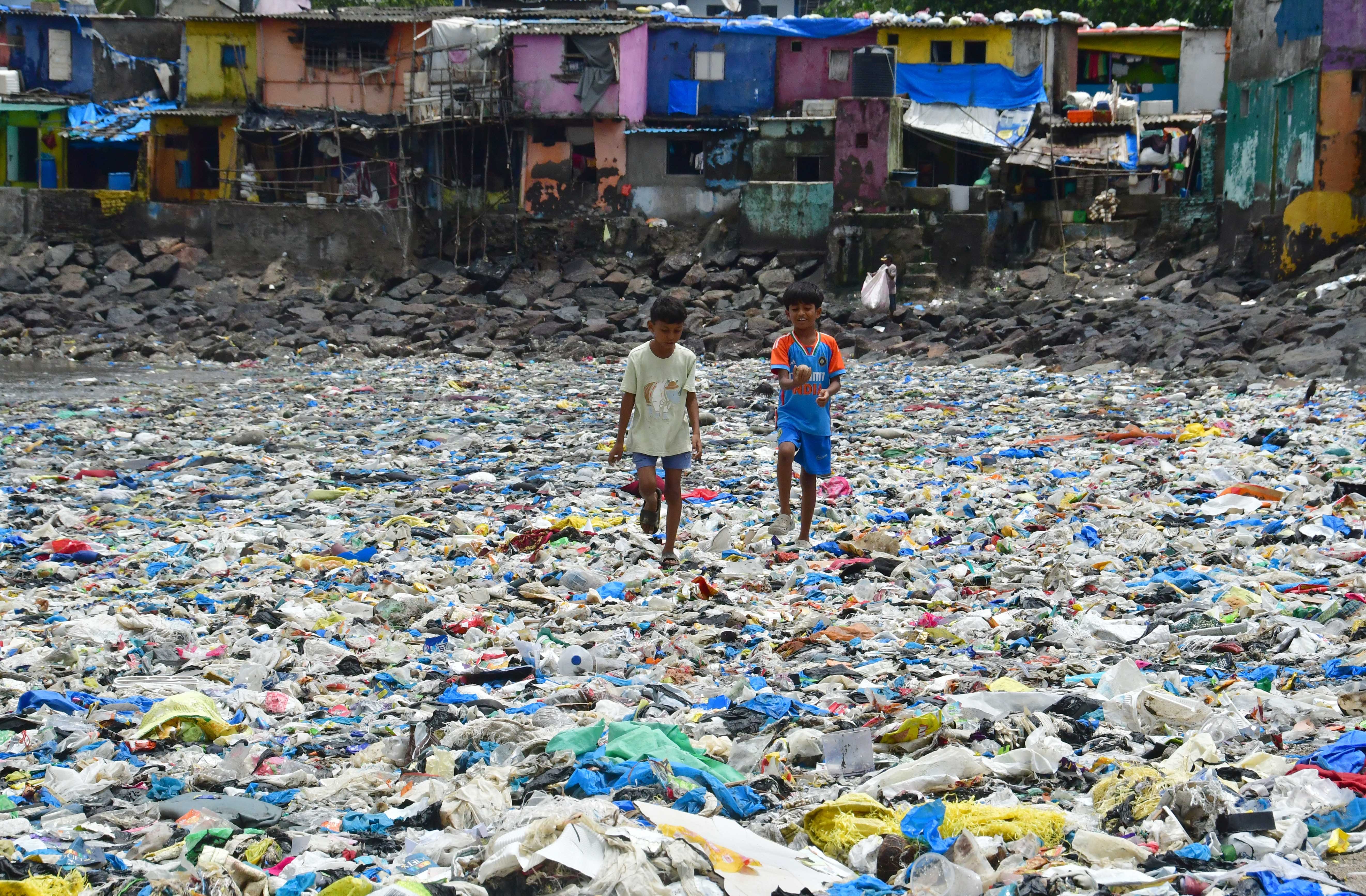 Two children walk across a flat stretch of shoreline that is completely covered in plastic waste.