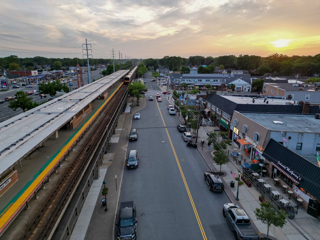 Aerial view of Massapequa Park, NY, showing Front St, the LIRR station, and surrounding businesses at sunset.