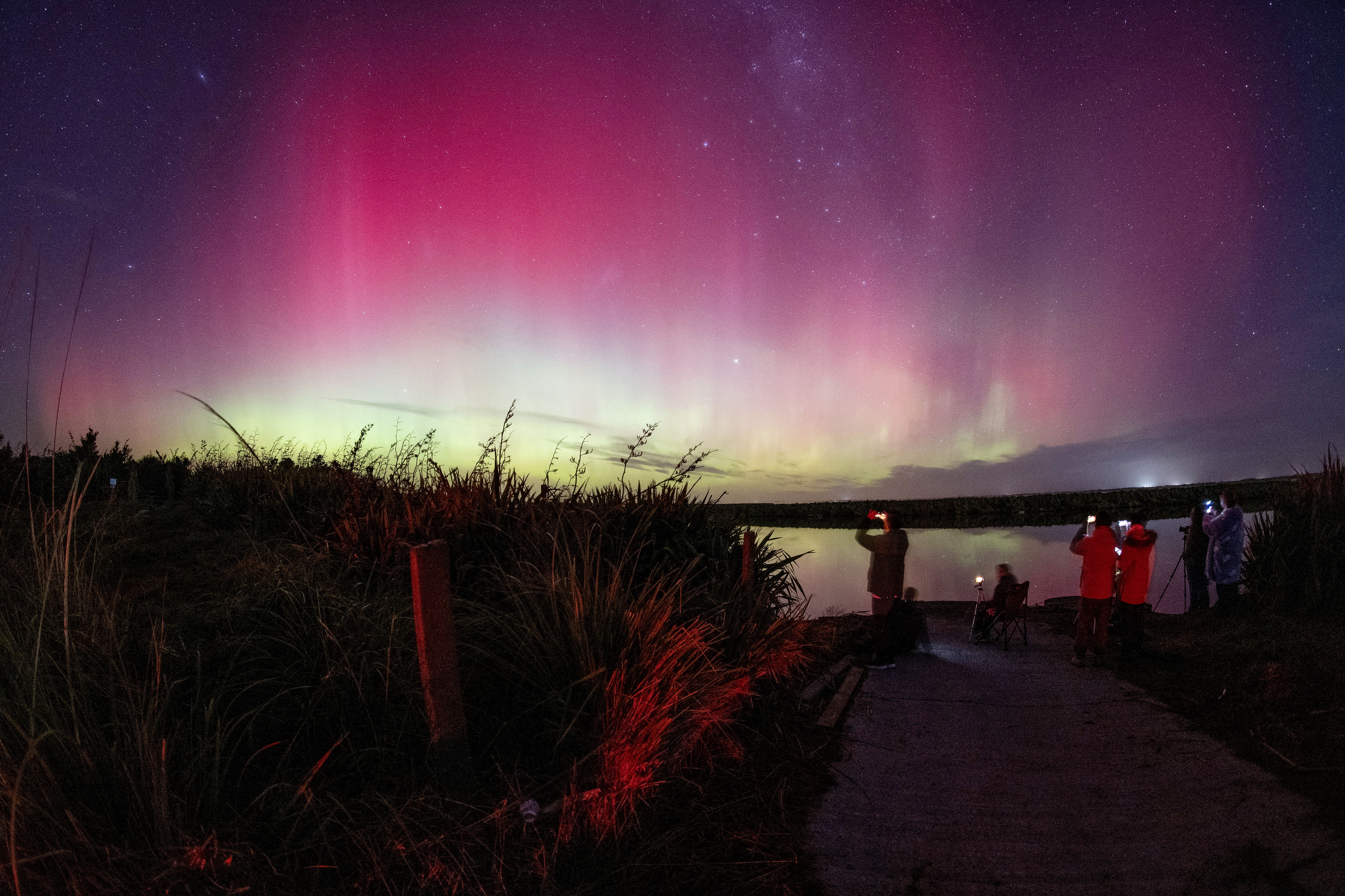 People take photos of the aurora australis, also known as the southern lights, as it glows on the horizon over Lake Ellesmere, on the outskirts of Christchurch, New Zealand, on June 1, 2025.