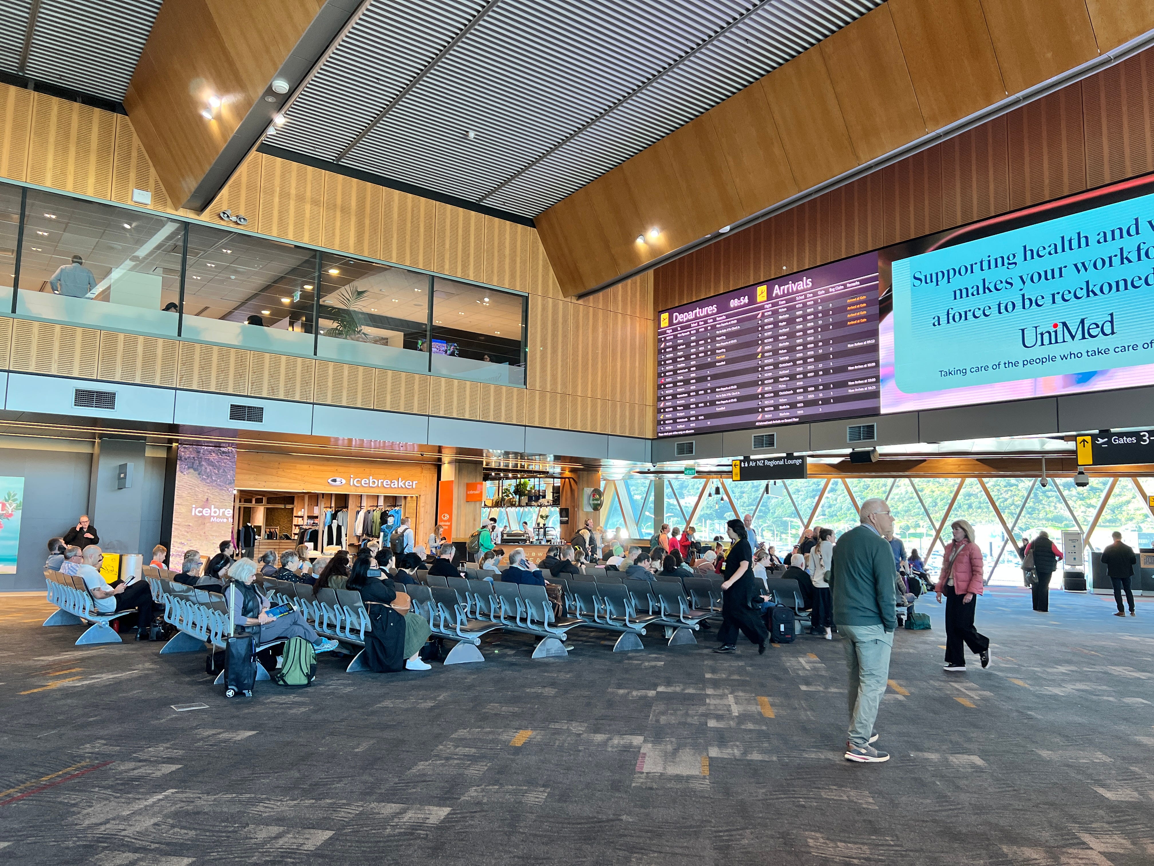 Airport waiting area in New Zealand with rows of chairs, large screens