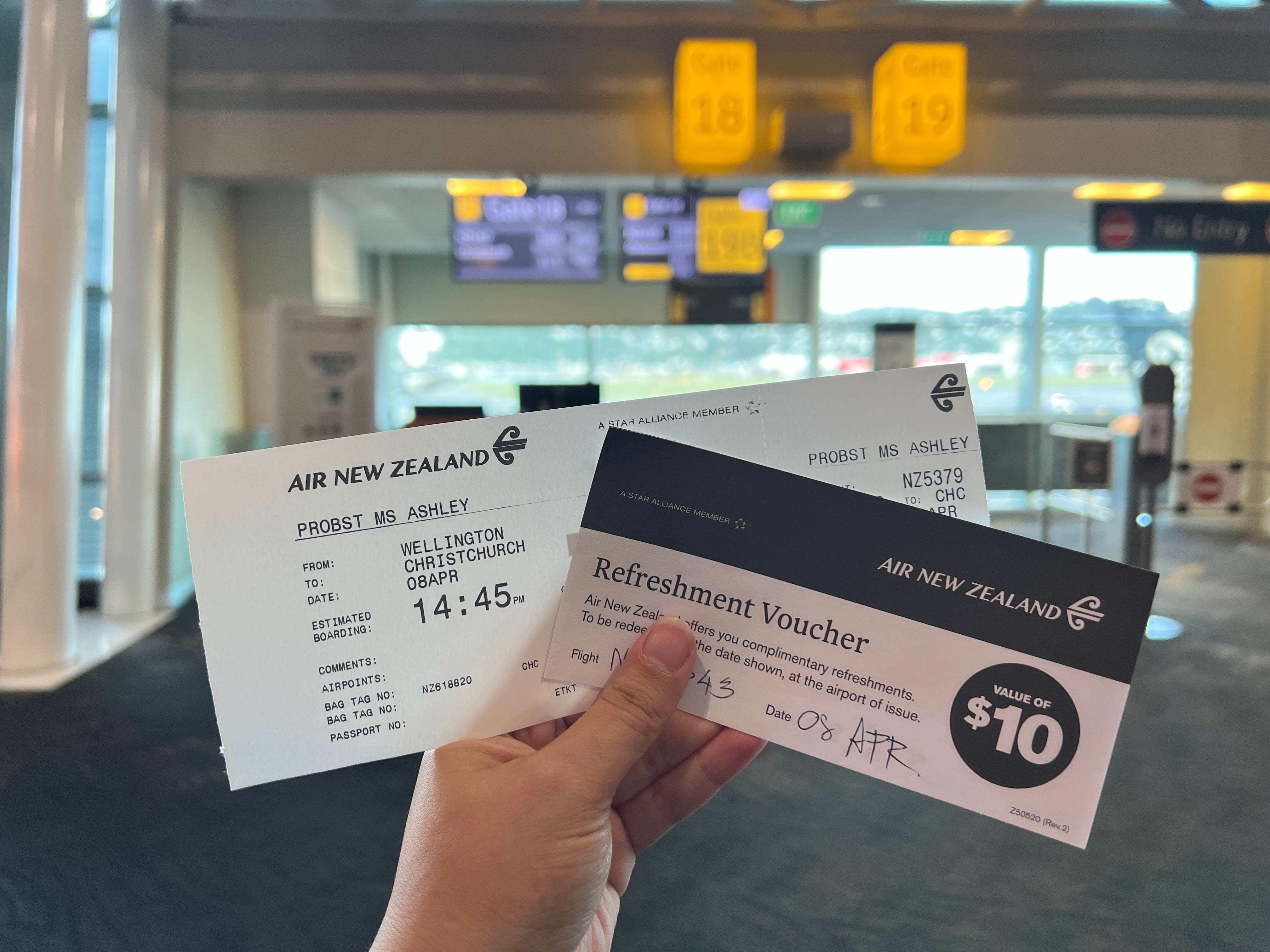Hand holding plane ticket and Air New Zealand $10 refreshment voucher
