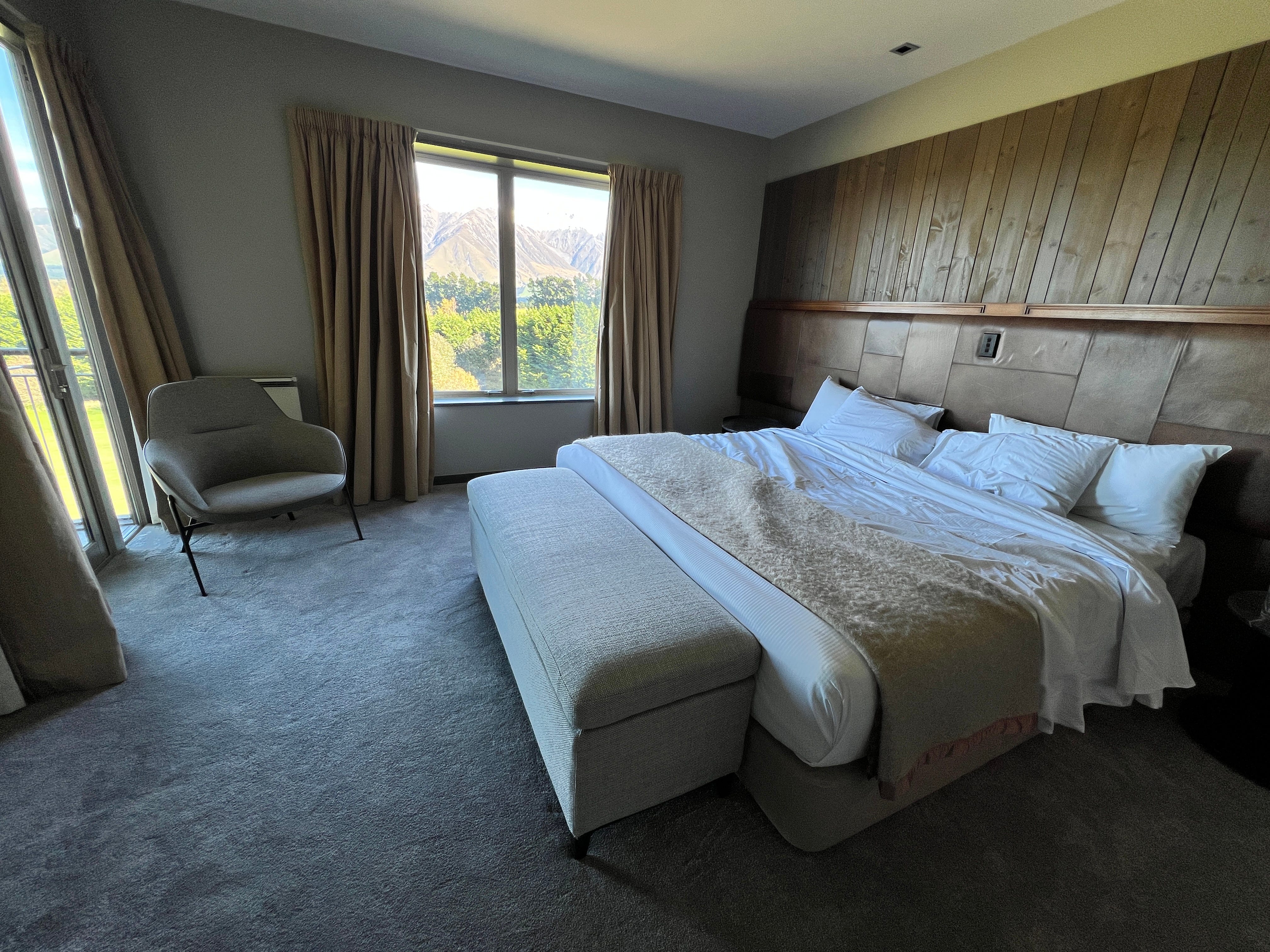 Large bed in front of wood-paneled wall with windows beside it featuring mountain views