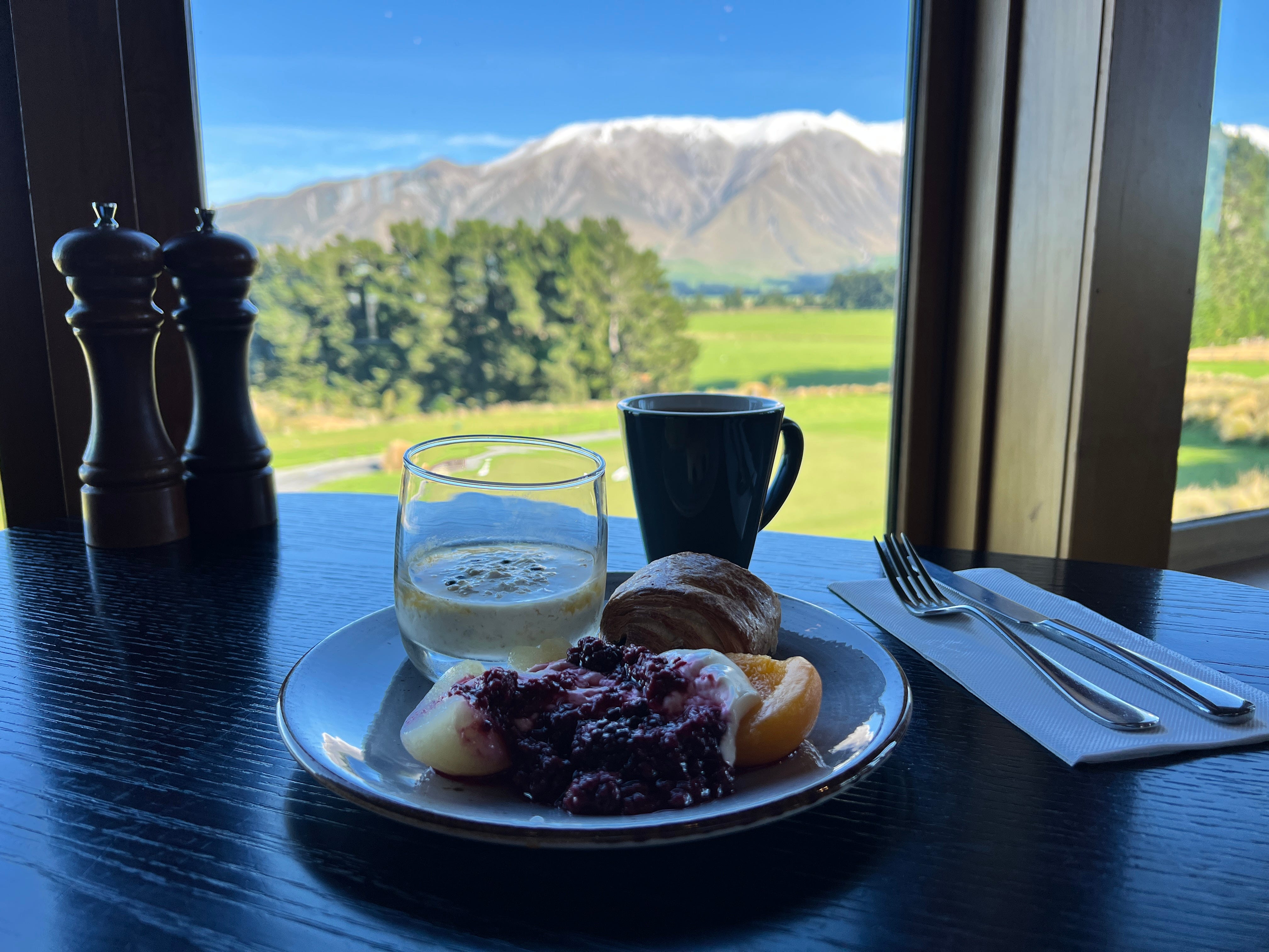 Coffee, fruit, croissant on table in front of window with mountain views