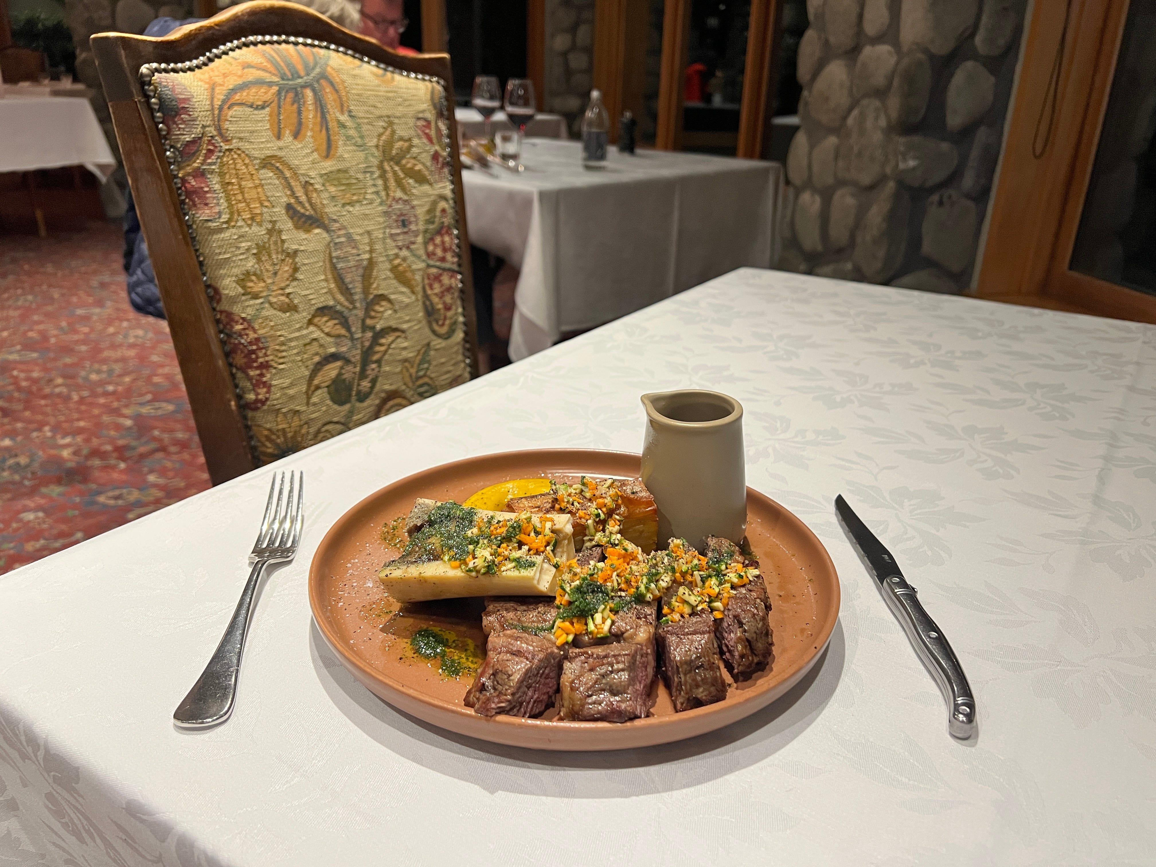Tablecloth-covered table with steak, bread, fork, knife