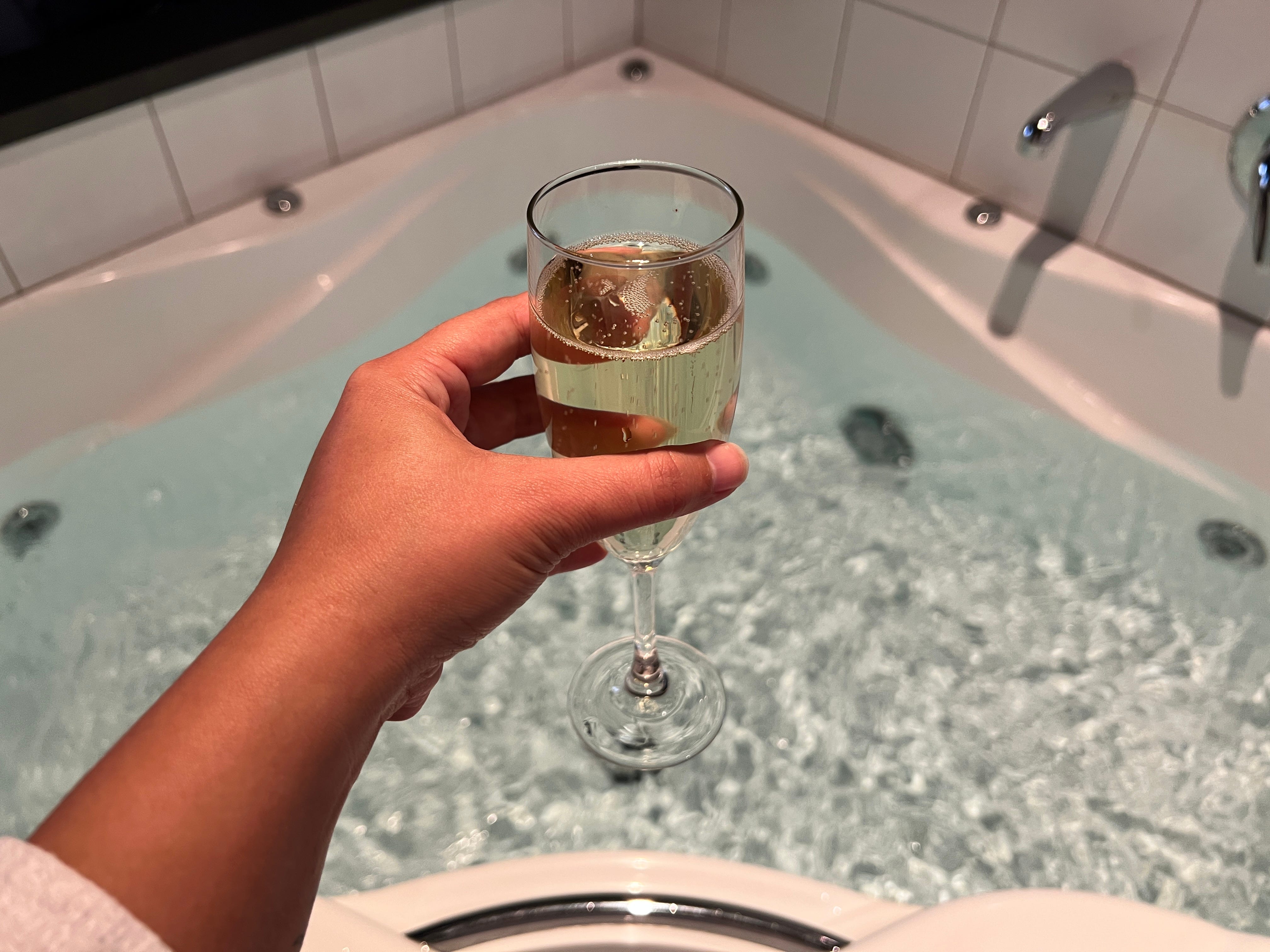 Glass of bubbly in hand above a full bathtub