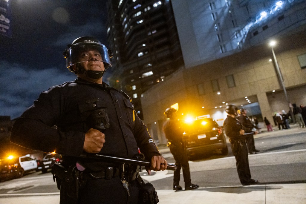 Police officer in riot gear stands guard during a protest at night.