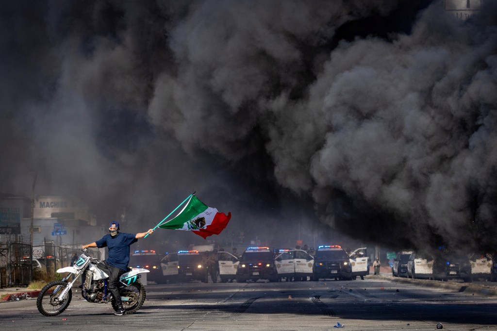 A man on a motorcycle waves a Mexican flag during a standoff between protesters and law enforcement in Los Angeles County.