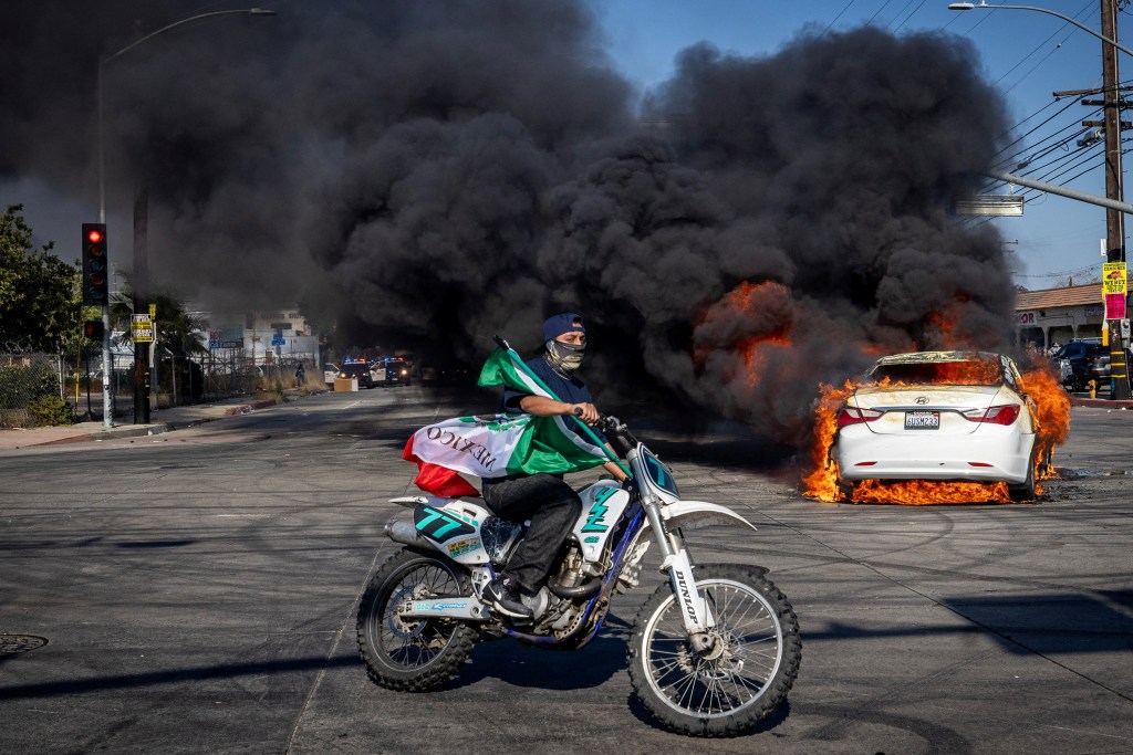 A burning car and a motorcyclist carrying a Mexican flag during a protest in Los Angeles County.