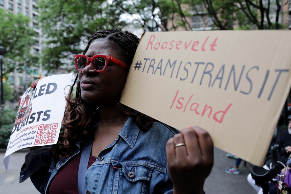 Protestor holding signs advocating for Roosevelt Island transit priority.