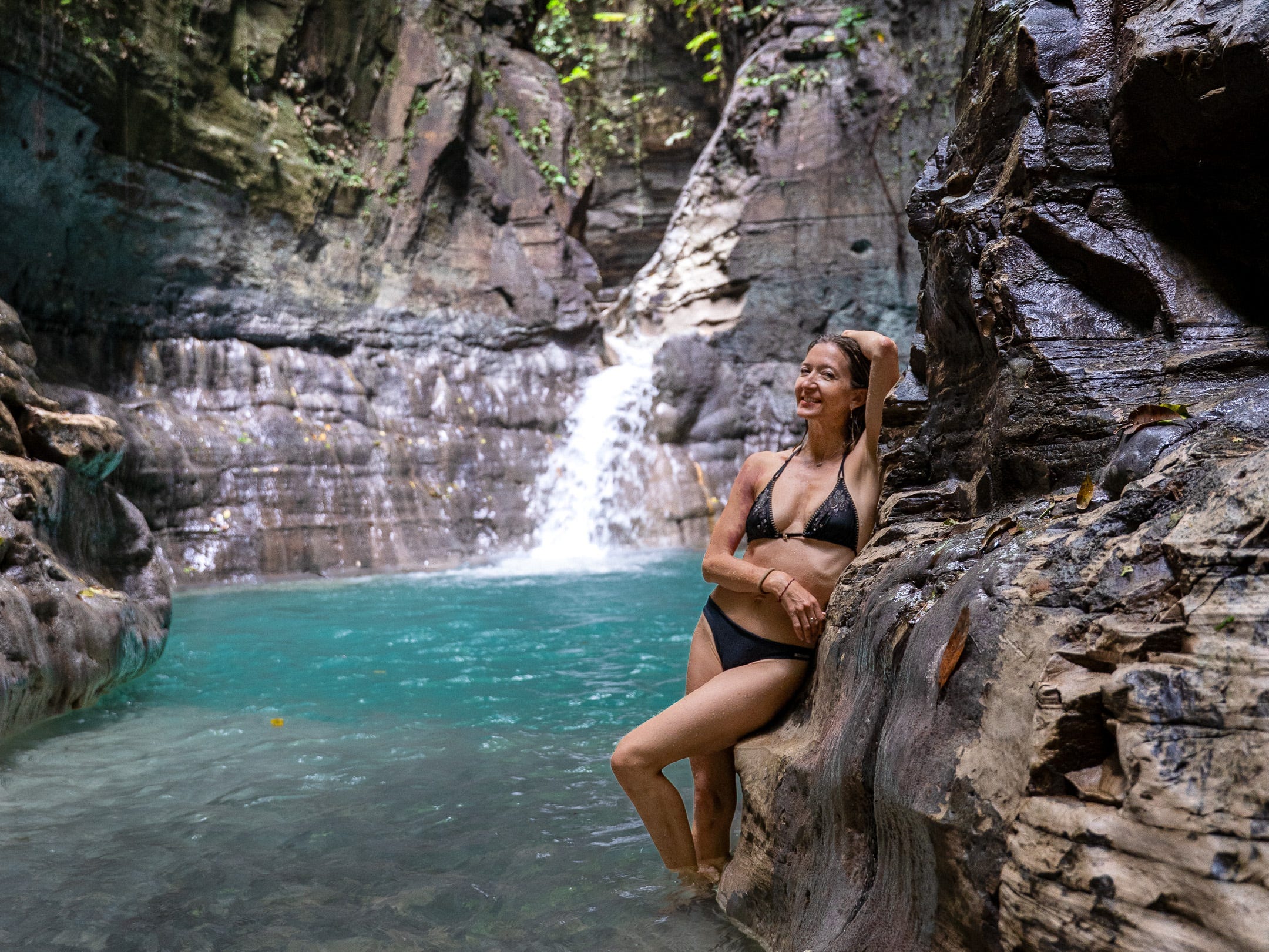 Woman standing in a bikini under a waterfall in Sumba, Indonesia.