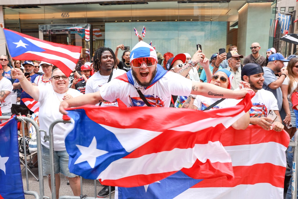 Spectators waving Puerto Rican flags at a parade.