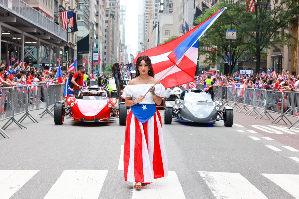 Woman in Puerto Rican flag attire carries a large flag during a parade.