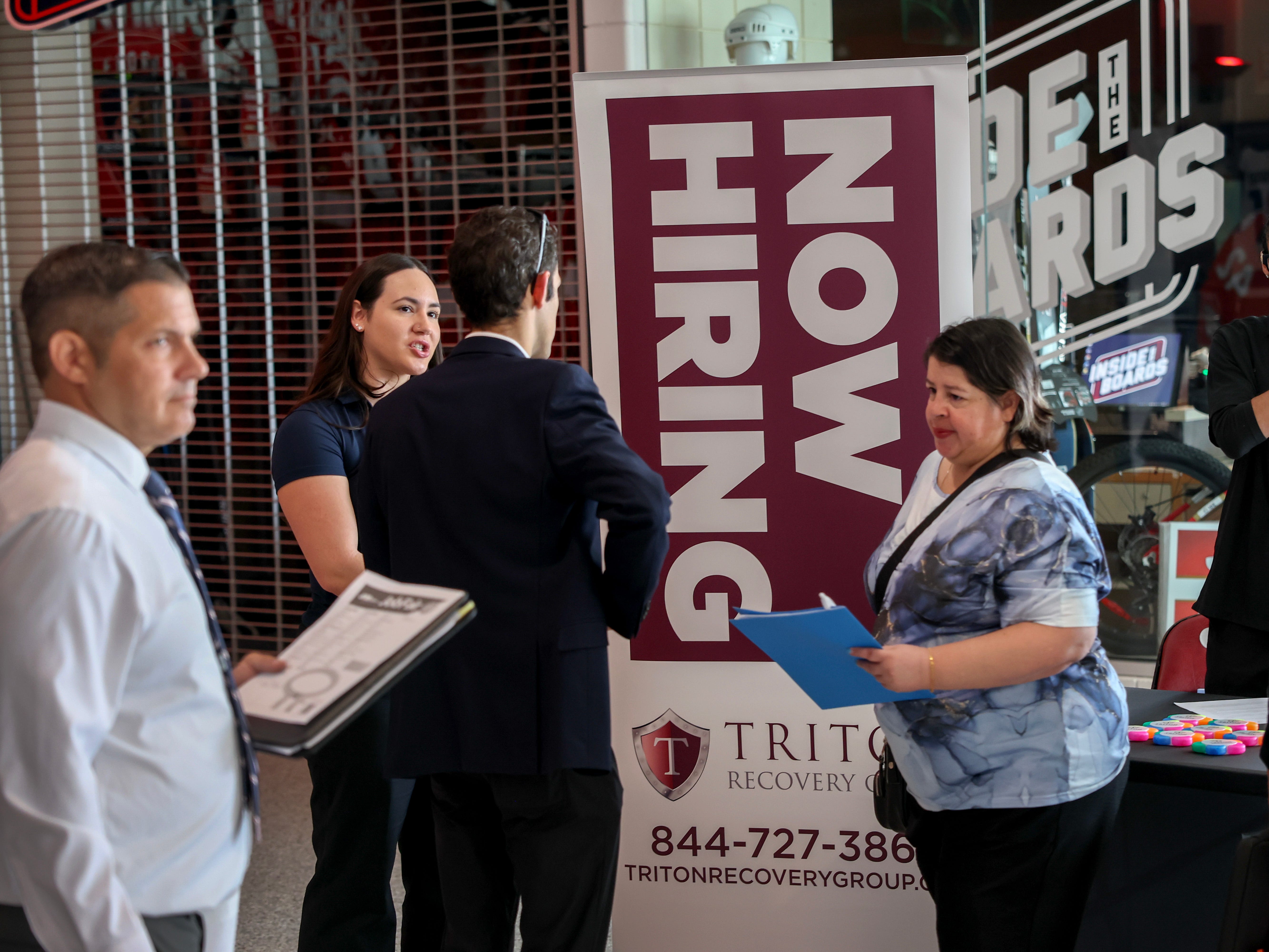 A "Now hiring" sign with four people in front of it.