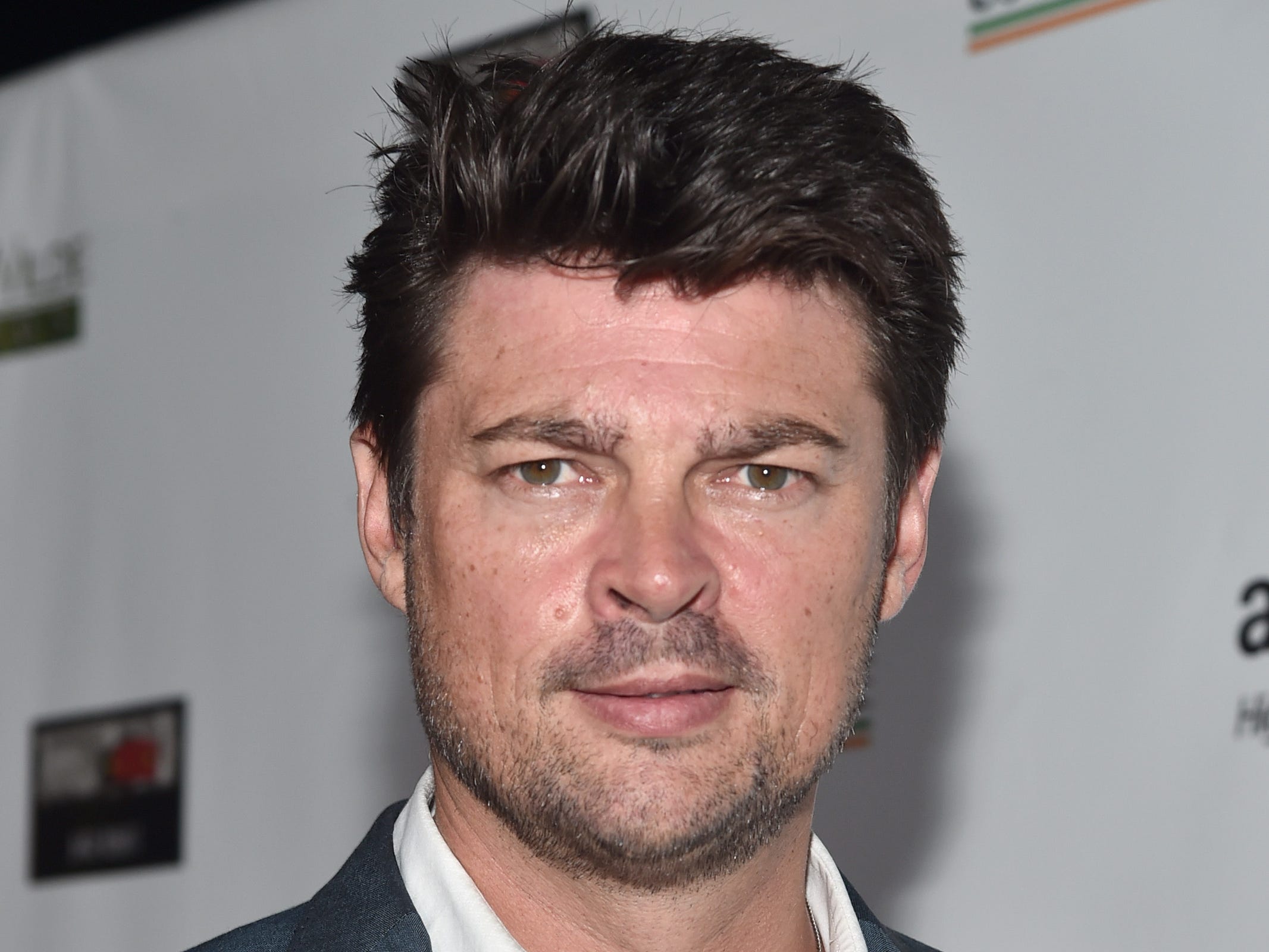 karl urban in a gray suit in front of a white background