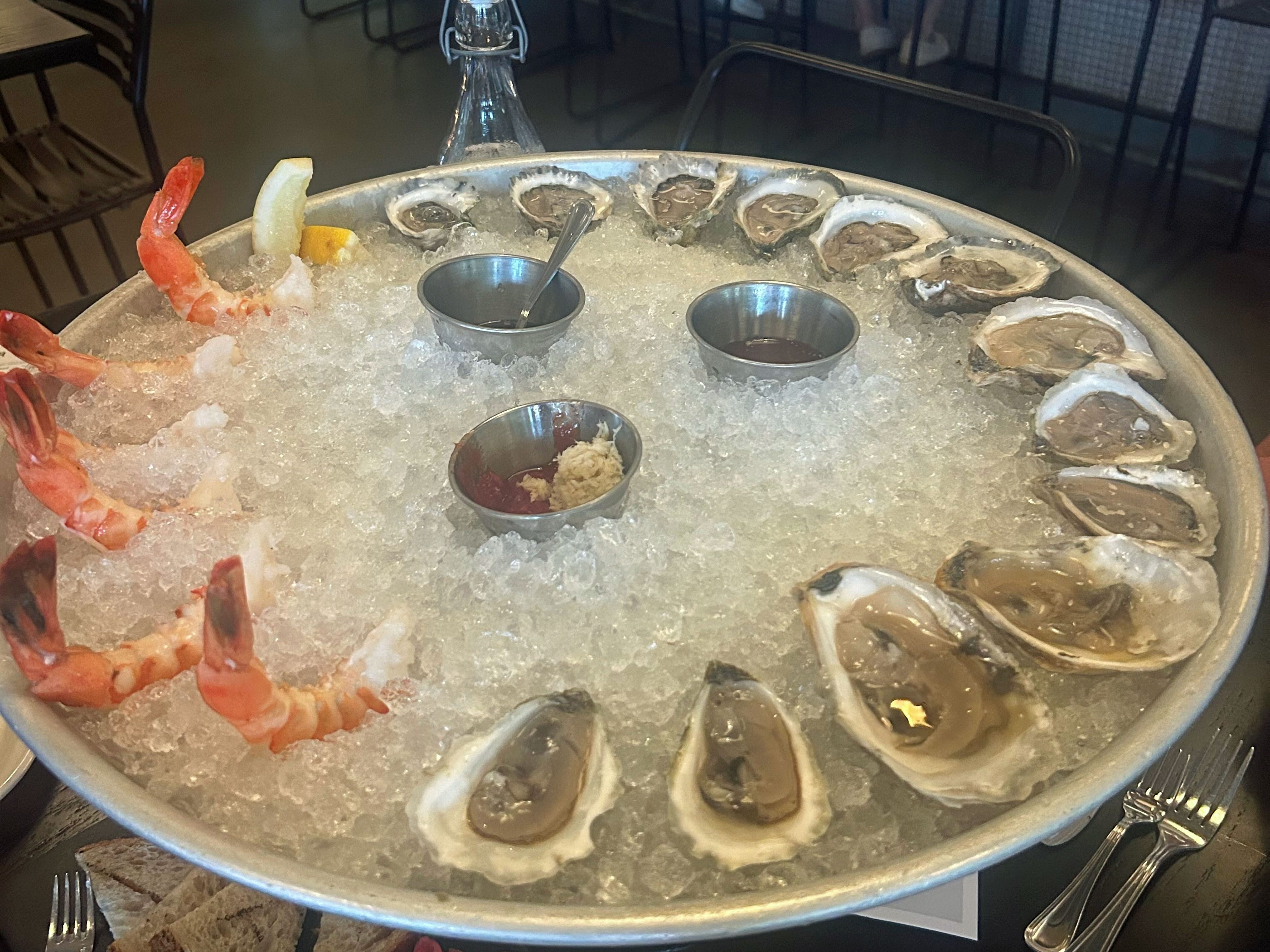 A large bowl of oysters and shrimp over ice with three sauces in the middle.