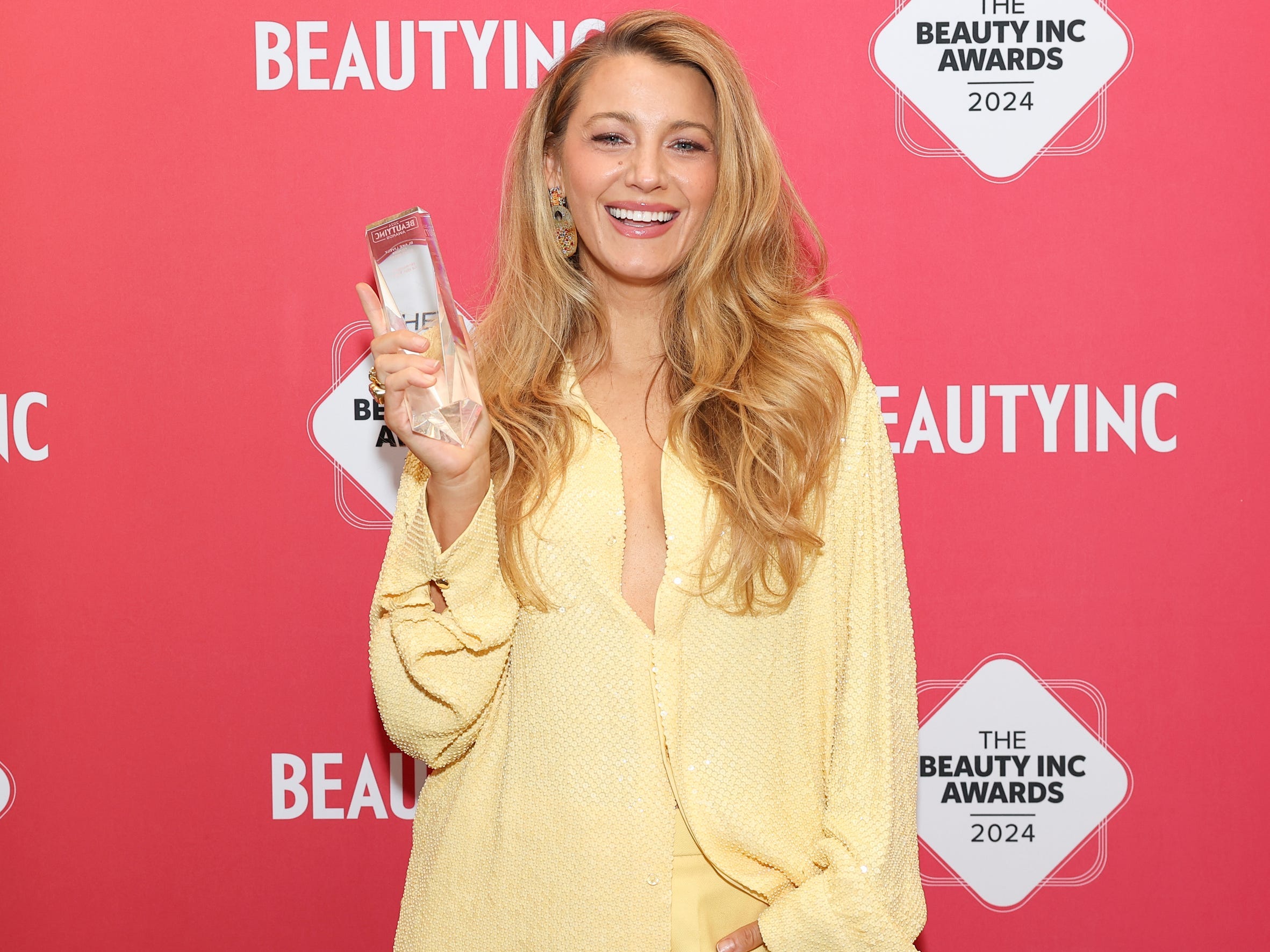 Blake Lively wearing a yellow shirt and holding a clear glass award at the Beauty Inc Awards 2024.