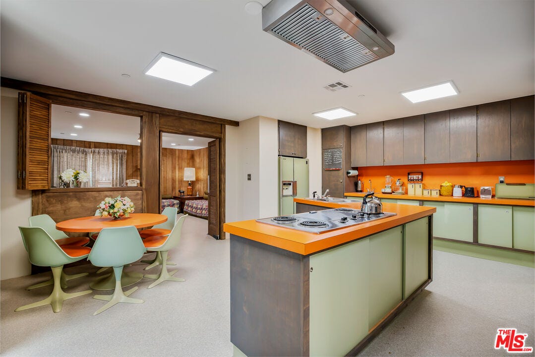 A kitchen with orange countertops and light green cupboards and chairs.