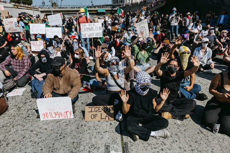 Protesters hold signs and raise their hands during a sit-in protest on a Los Angeles freeway on June 8, 2025. Following a series of aggressive federal immigration operations in Los Angeles, tensions escalated when Immigration and Customs Enforcement (ICE) agents conducted a high-profile raid on a Home Depot location. The raid sparked widespread protests across the city, where demonstrators decried the targeting of immigrant communities and the separation of families. Clashes soon broke out between protesters and federal agents, prompting U.S. President Donald Trump to deploy 2,000 National Guard troops to the city, a move harshly criticized by California officials, including the governor, as "purposefully inflammatory." (Photo by David Pashaee / Middle East Images via AFP) (Photo by DAVID PASHAEE/Middle East Images/AFP via Getty Images)