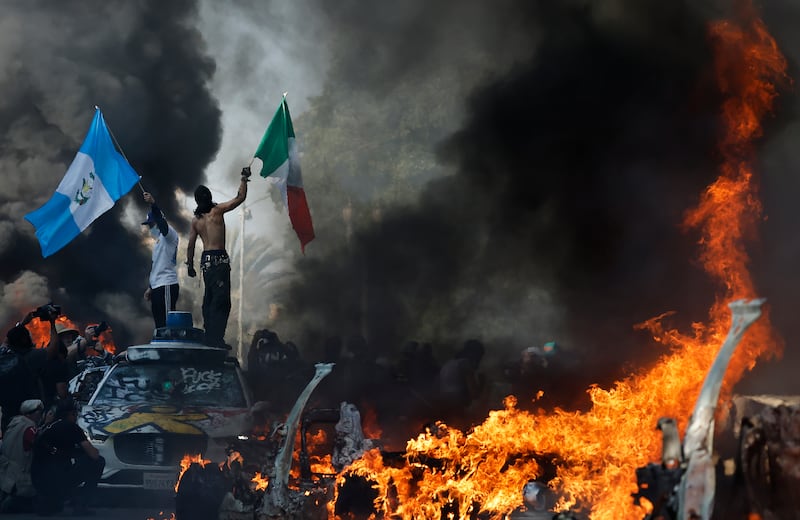 LOS ANGELES, CALIFORNIA - JUNE 08: Protestors wave flags as burning and vandalized Waymo cars line the street on June 08, 2025 in Los Angeles, California. Tensions in the city remain high after the Trump administration called in the National Guard against the wishes of city leaders following two days of clashes with police during a series of immigration raids. (Photo by Mario Tama/Getty Images)