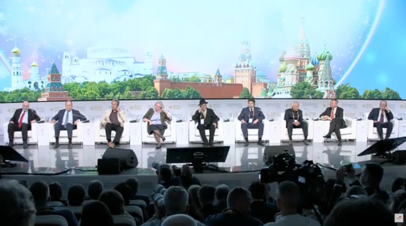 A group of people in chairs in front of a painted background of the Kremlin and Russian churches