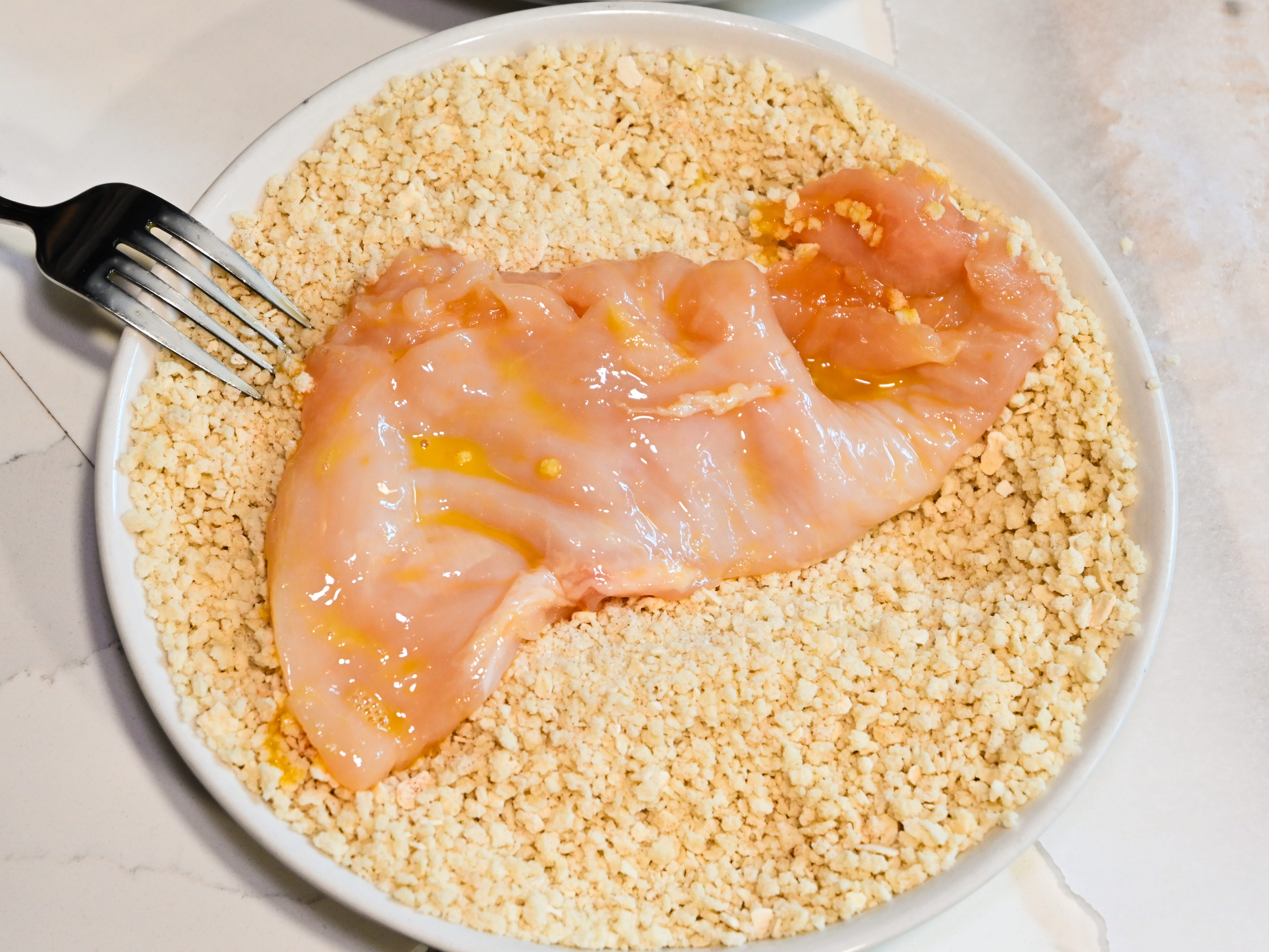 A chicken breast, covered in the egg wash, in the bowl of panko.