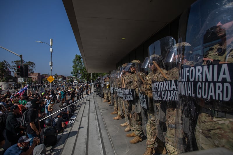 Demonstrators holding signs and flags face California National Guard members standing guard outside the Federal Building as they protest in response to federal immigration operations in Los Angeles, on June 9, 2025.