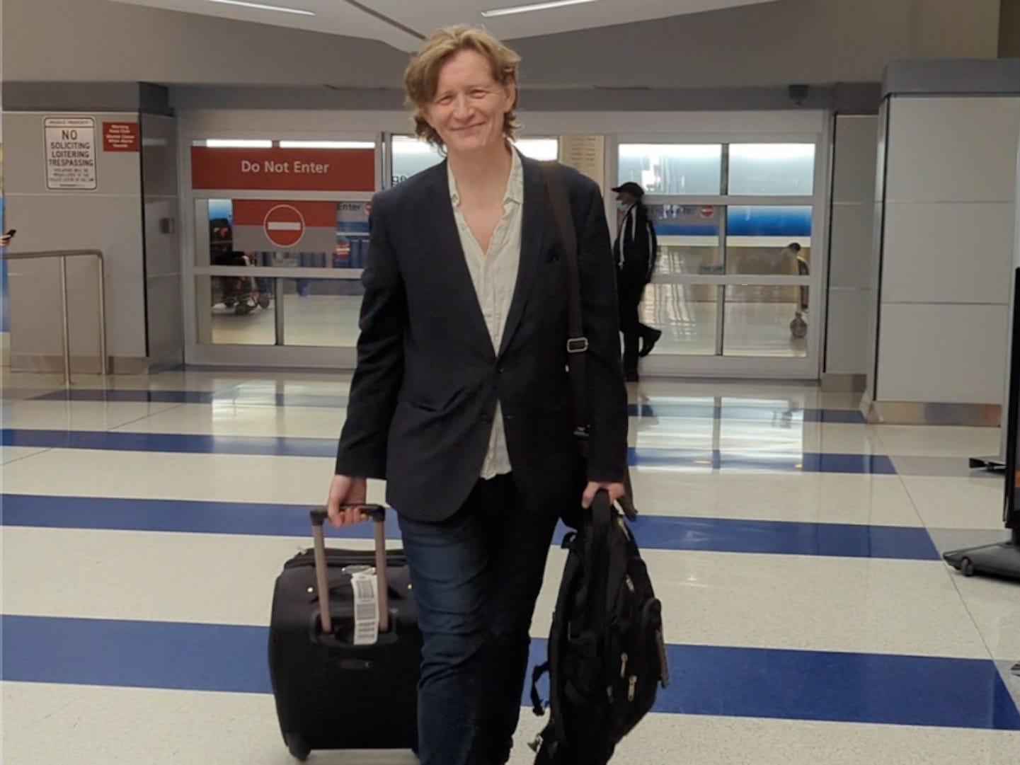 A man pulls a suitcase through the arrivals area of an airport.