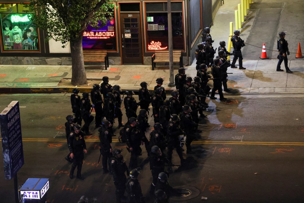 Police officers in riot gear stand on a city street during a protest.