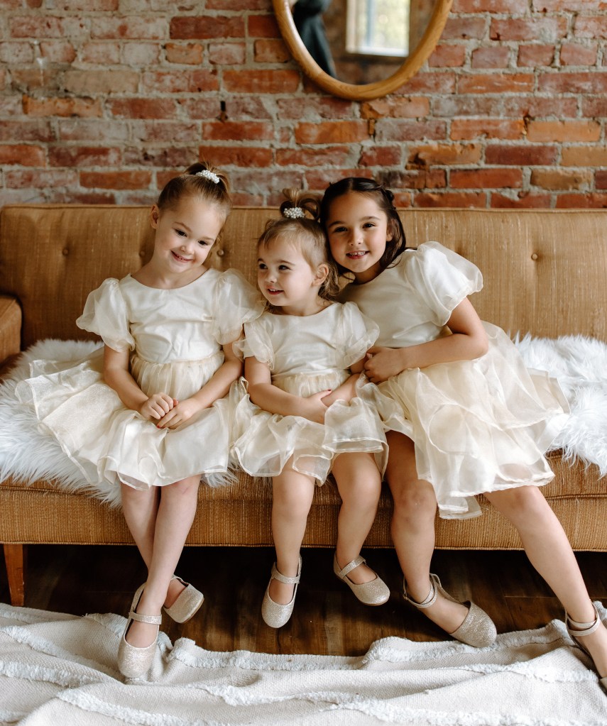 Three young sisters in matching dresses sitting on a couch.