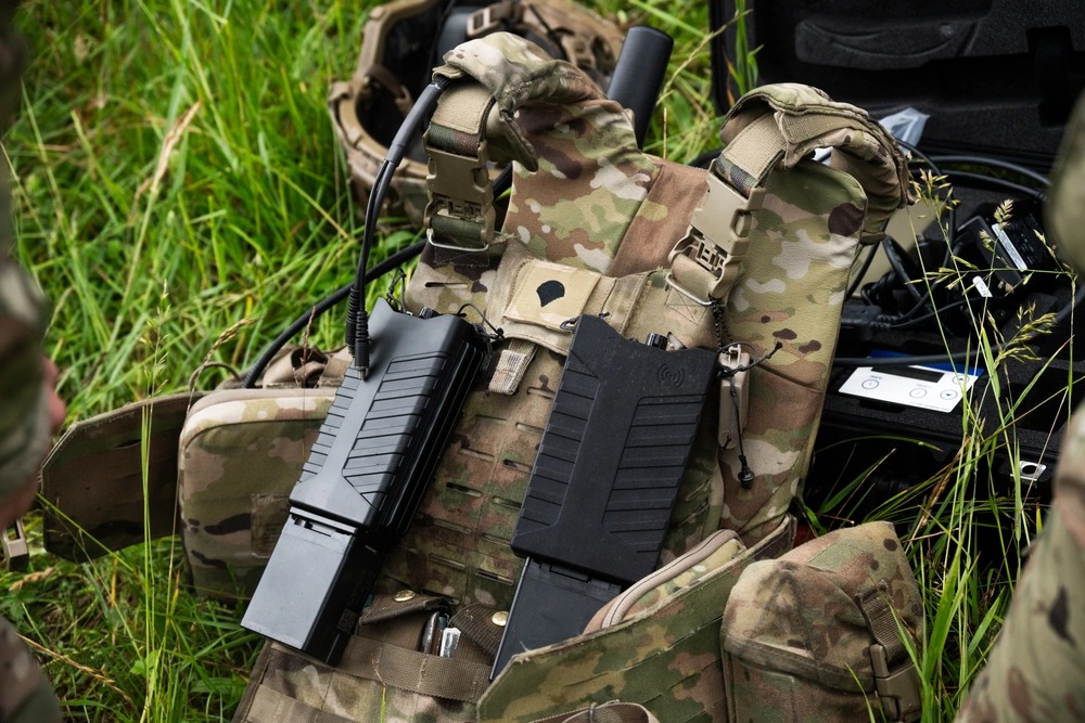 US Army equipment including two black devices attached to a camouflage vest.