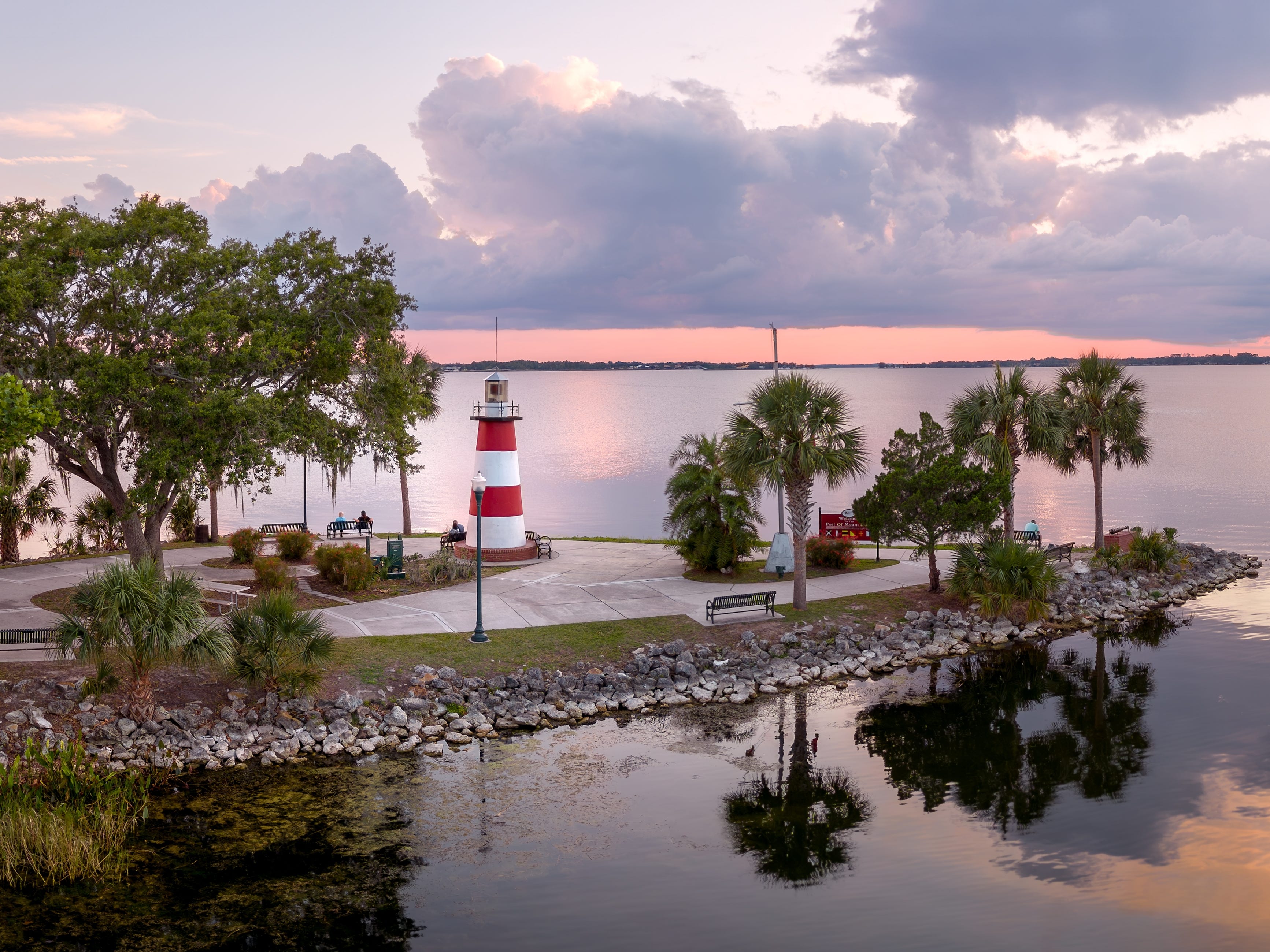 A lighthouse surrounded by trees and water at sunset.