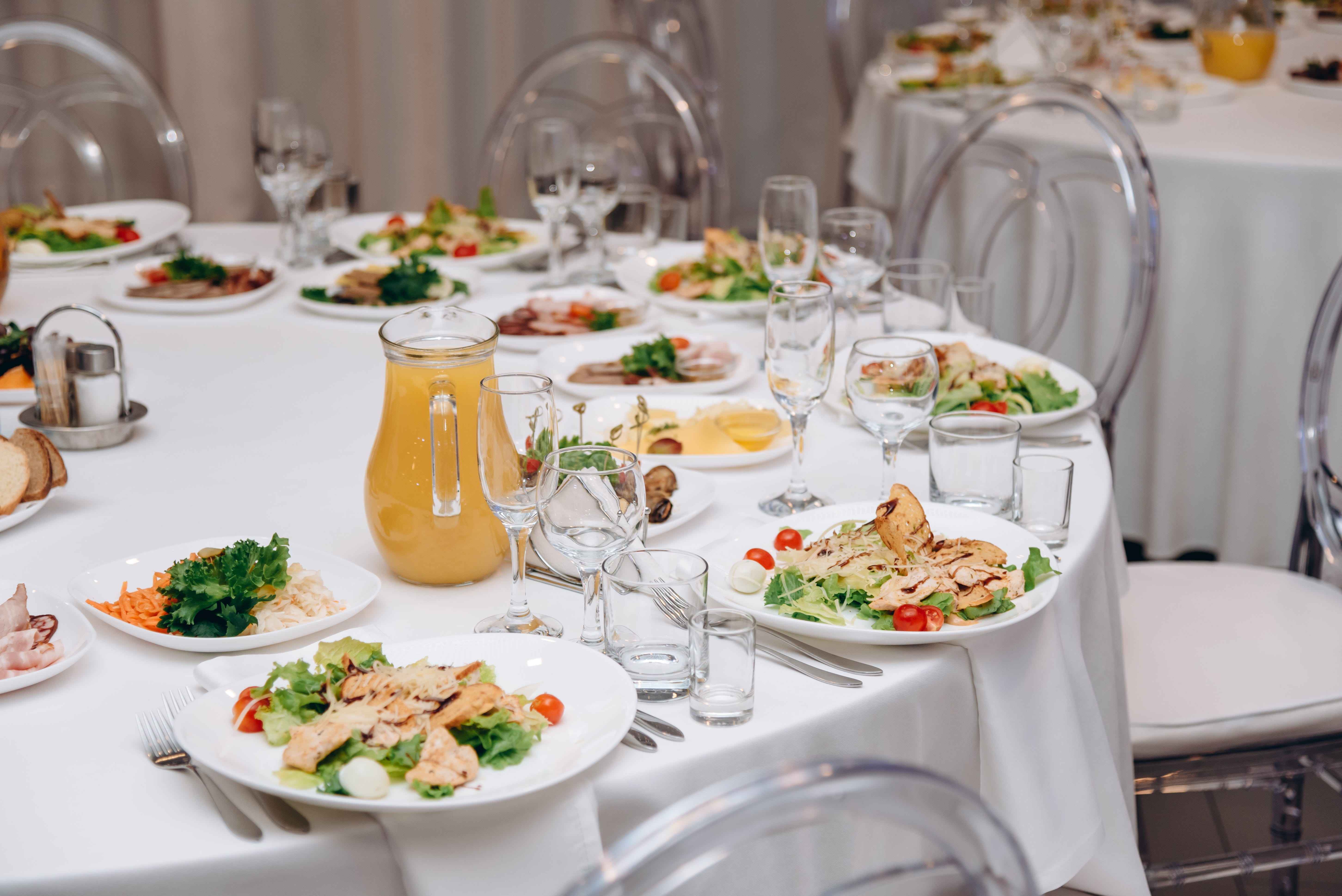 Table set with caesar salads, tablecloth-covered tables, and clear chairs