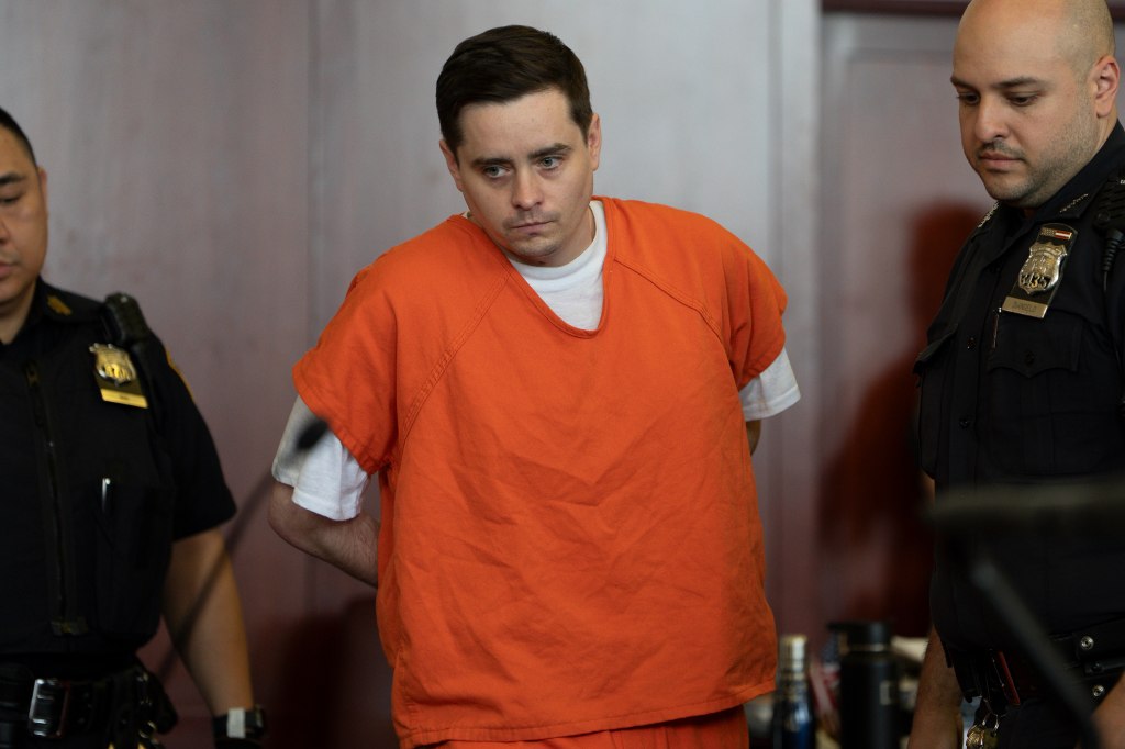 A man in an orange jumpsuit stands in a courtroom.