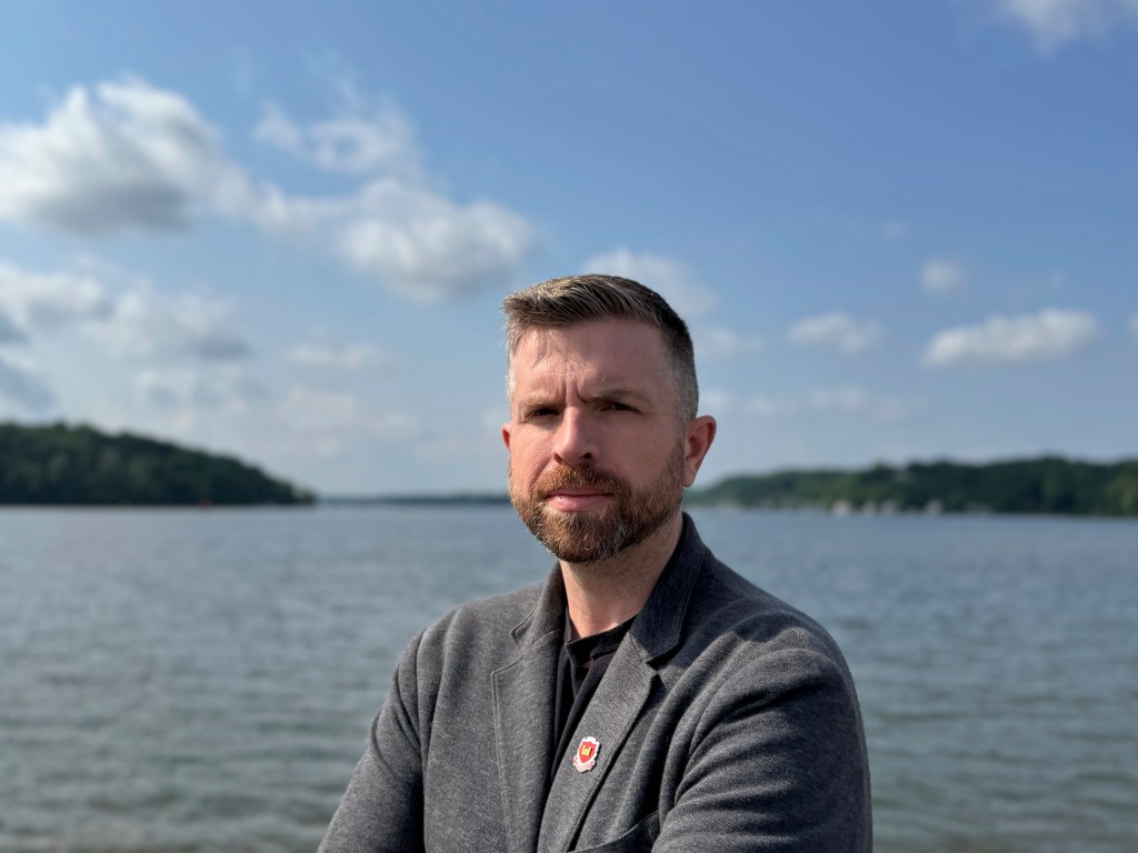 Portrait of a man in a gray jacket by a lake.