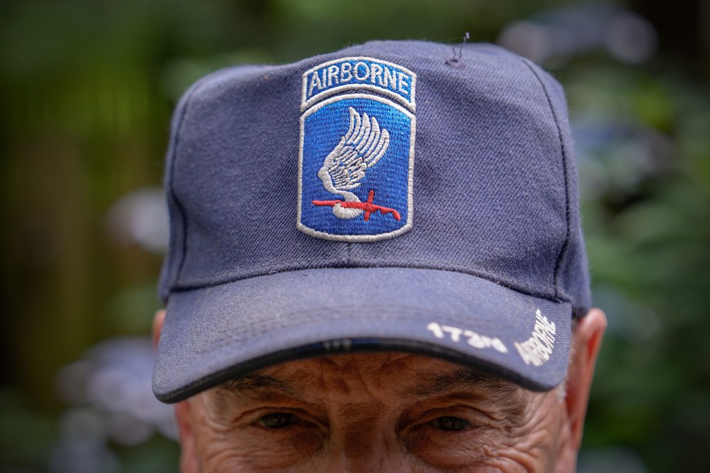 Close-up of a man's face partially obscured by a navy blue baseball cap with a 173rd Airborne Brigade patch.