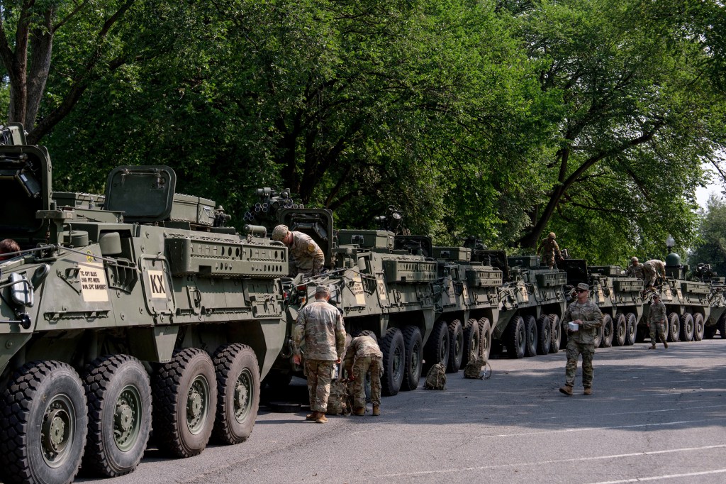 Military vehicles parked in a row with soldiers nearby.