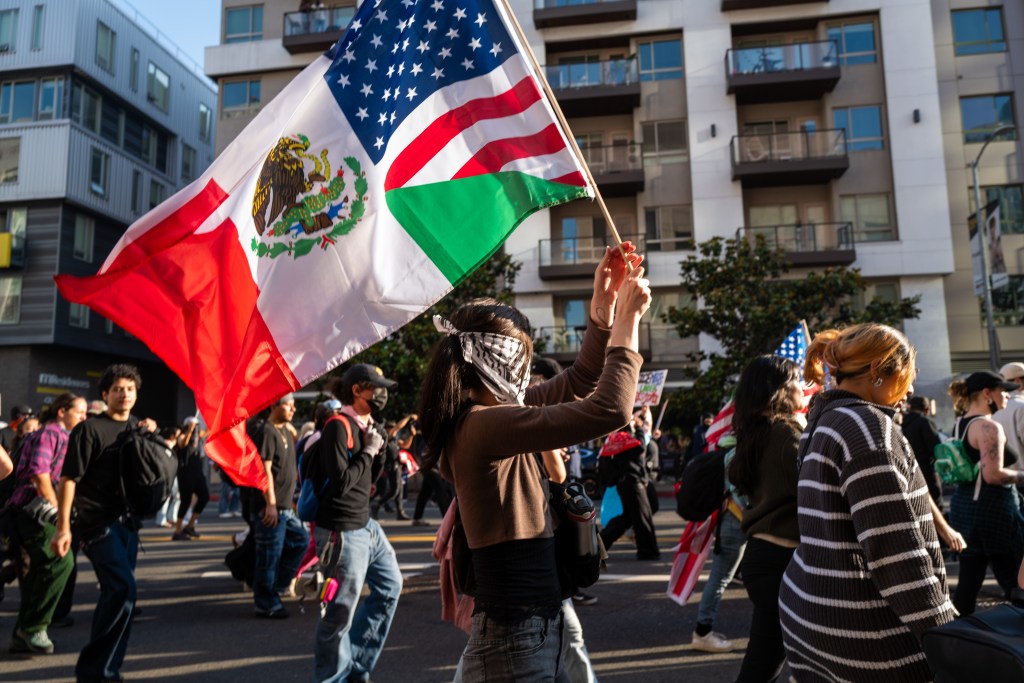 Protestors march holding Mexican and American flags.