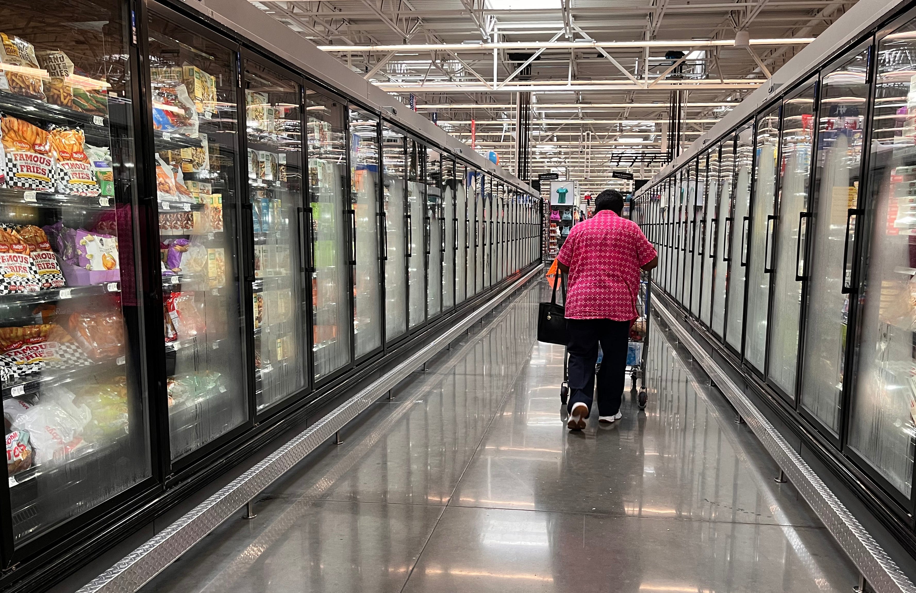 A person walking down a frozen section of a suermarket aisle.