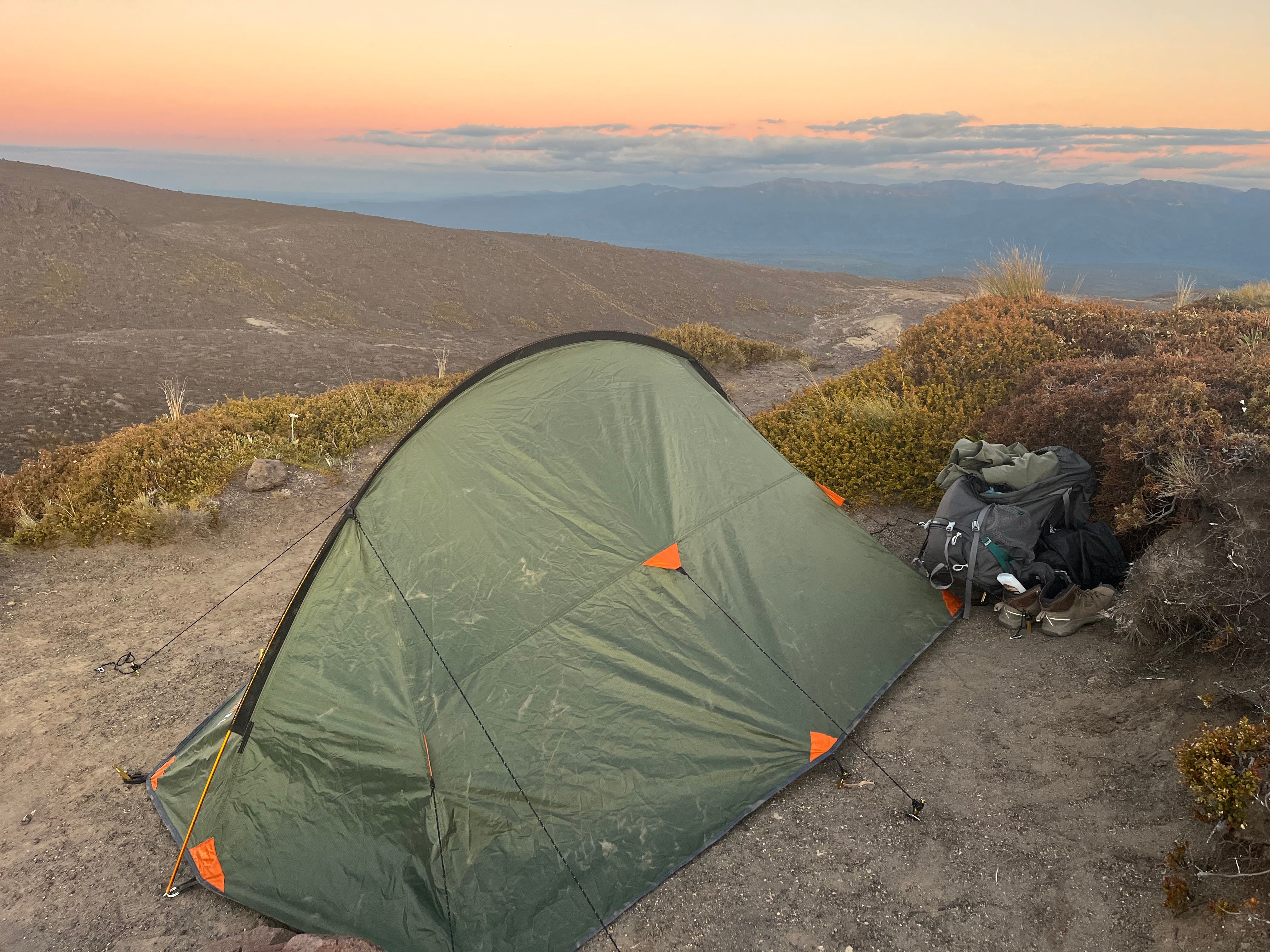 The author's camping setup during a hike in New Zealand, complete with a green tent and her backpack with supplies.
