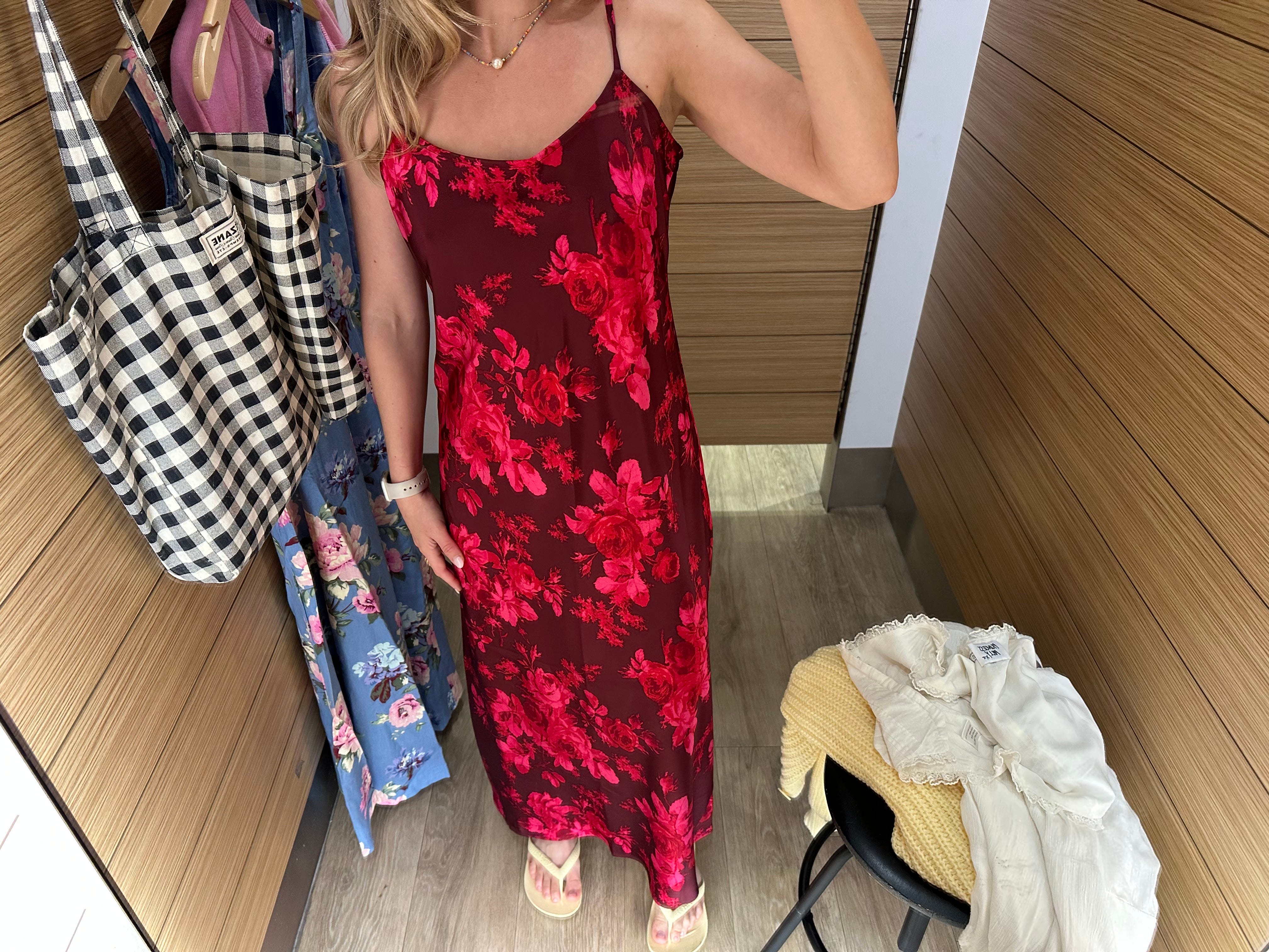 Chloe wears a red floral dress in a fitting room.