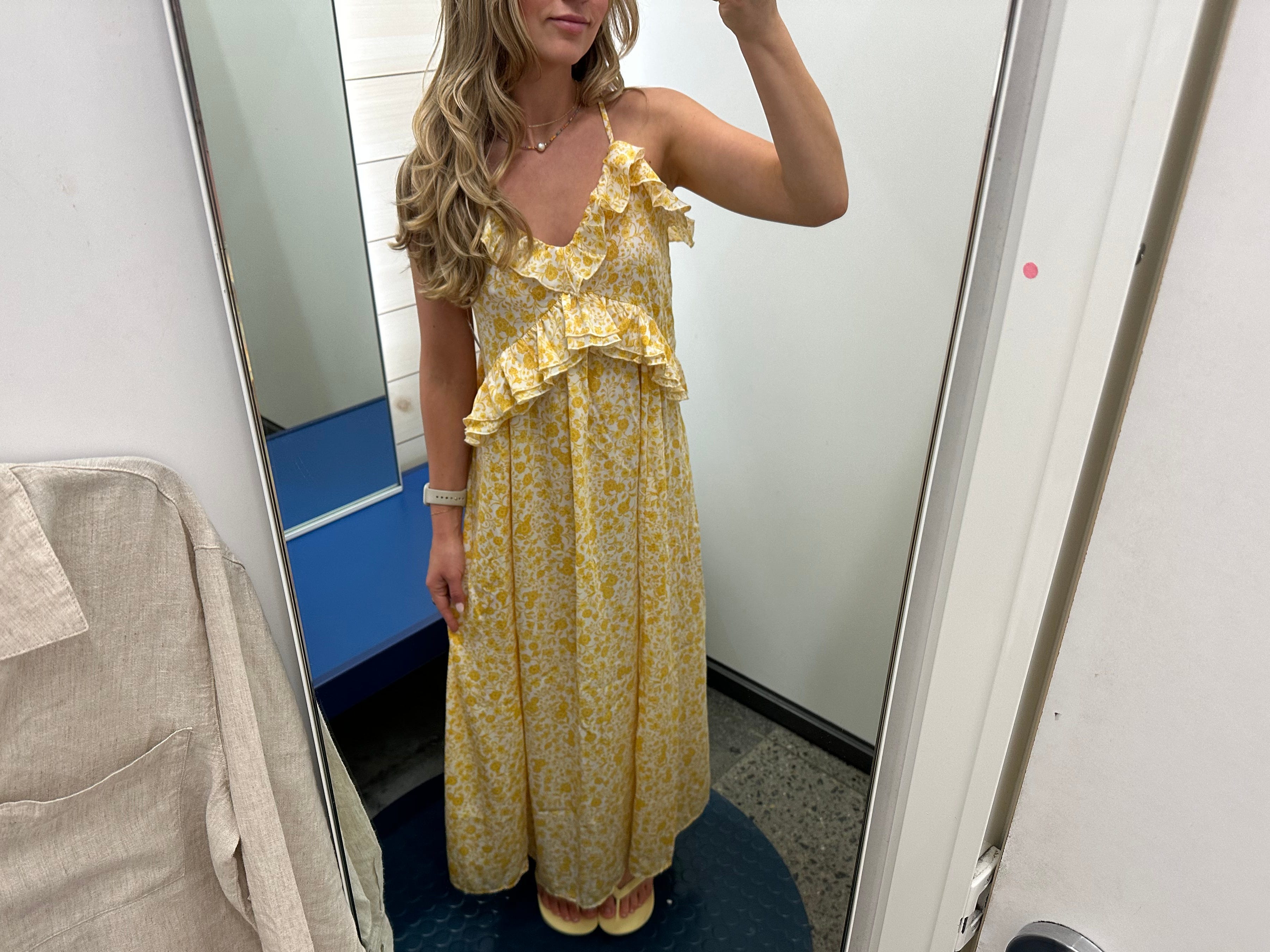 Chloe wears a yellow floral dress in a fitting room.
