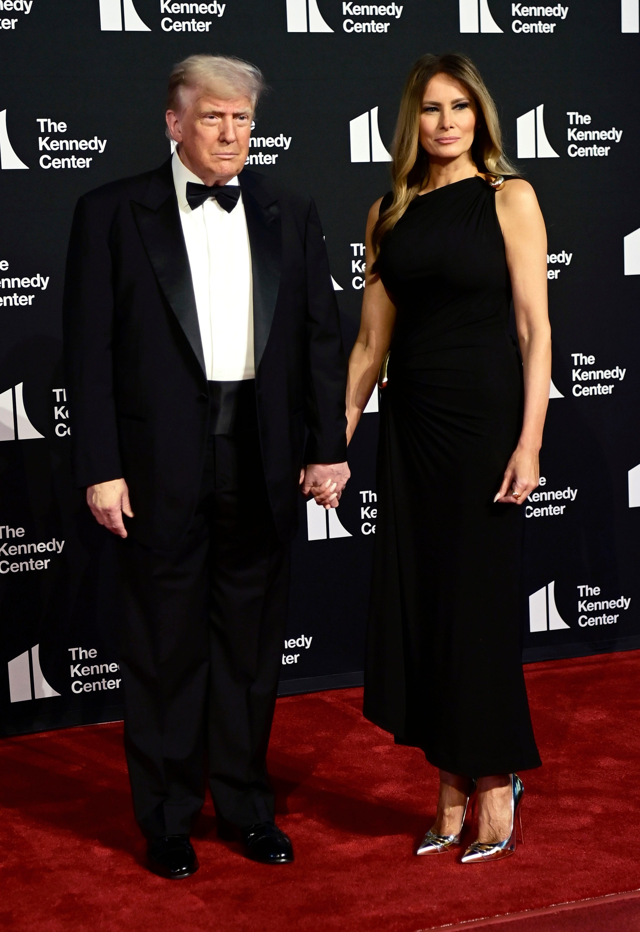 Donald and Melania Trump hold hands on a red carpet at the Kennedy Center.