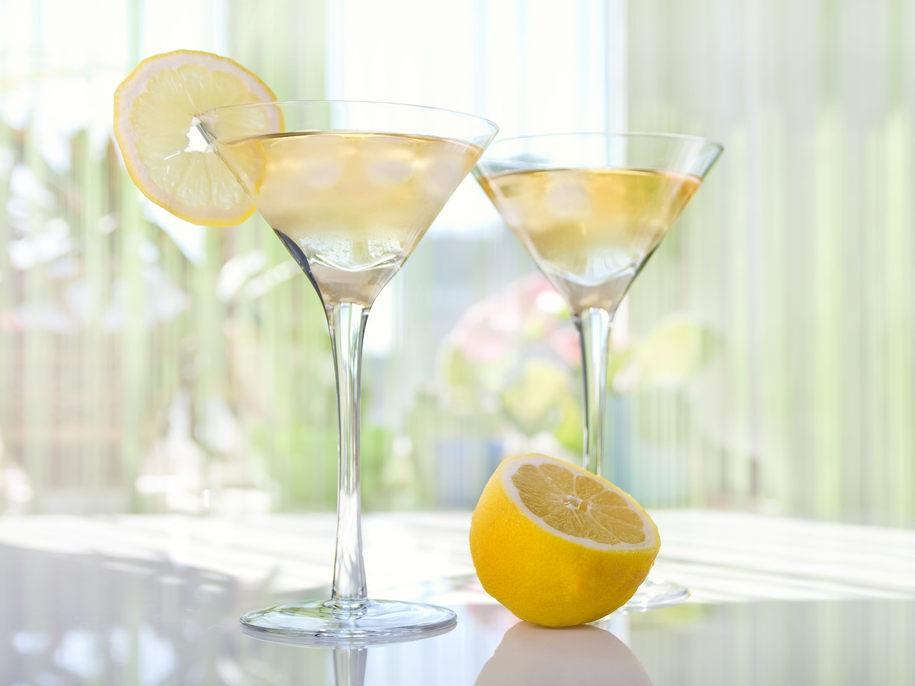 Lemon-drop martinis on a white surface with a lemon slice on the rim of one of the glasses.