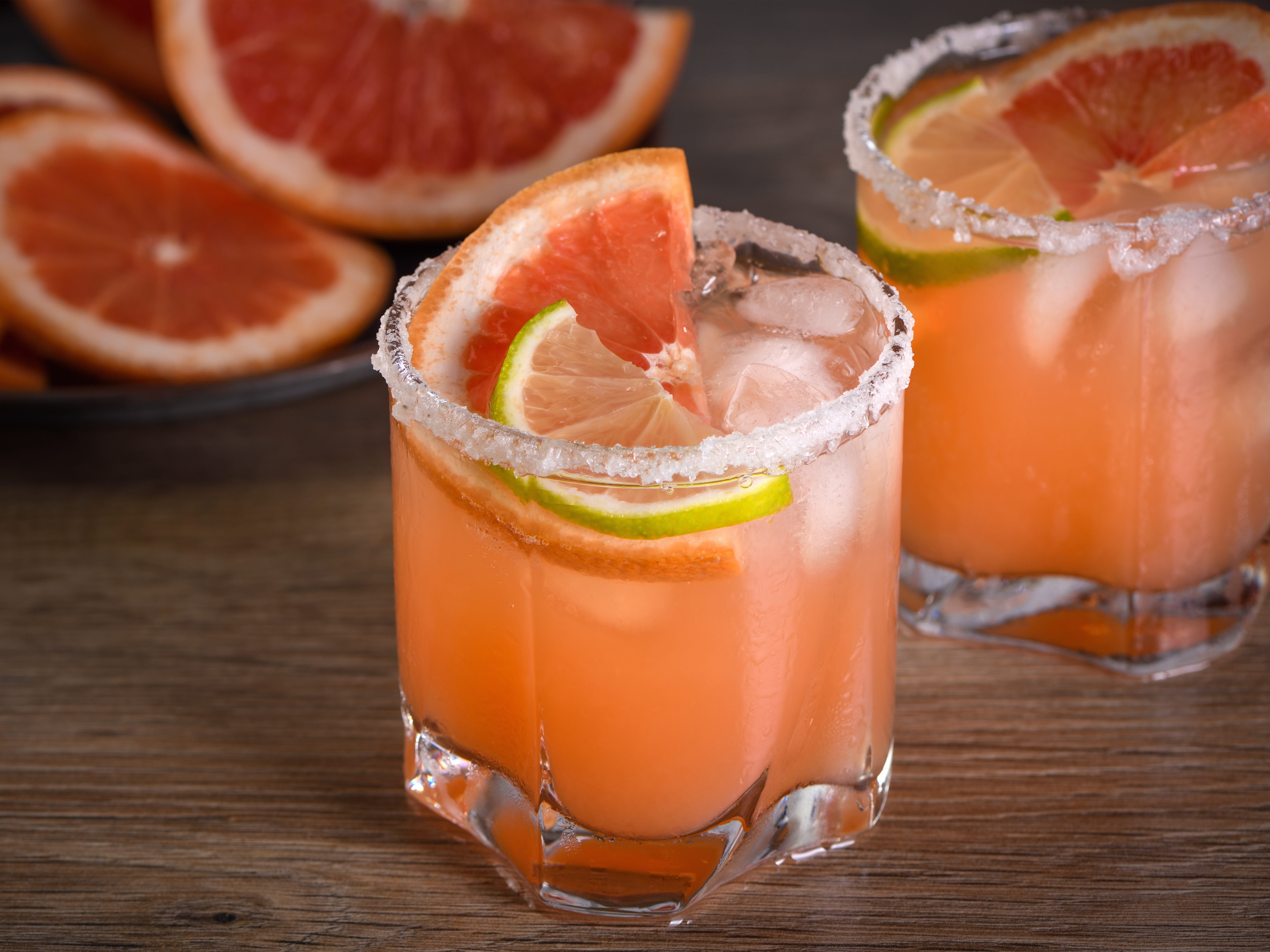 Two glasses of Paloma with slices of grapefruit and lime next to a plate of grapefruit slices.