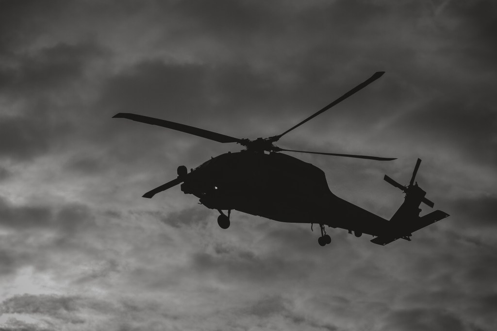 Black and white silhouette of a military helicopter in flight.