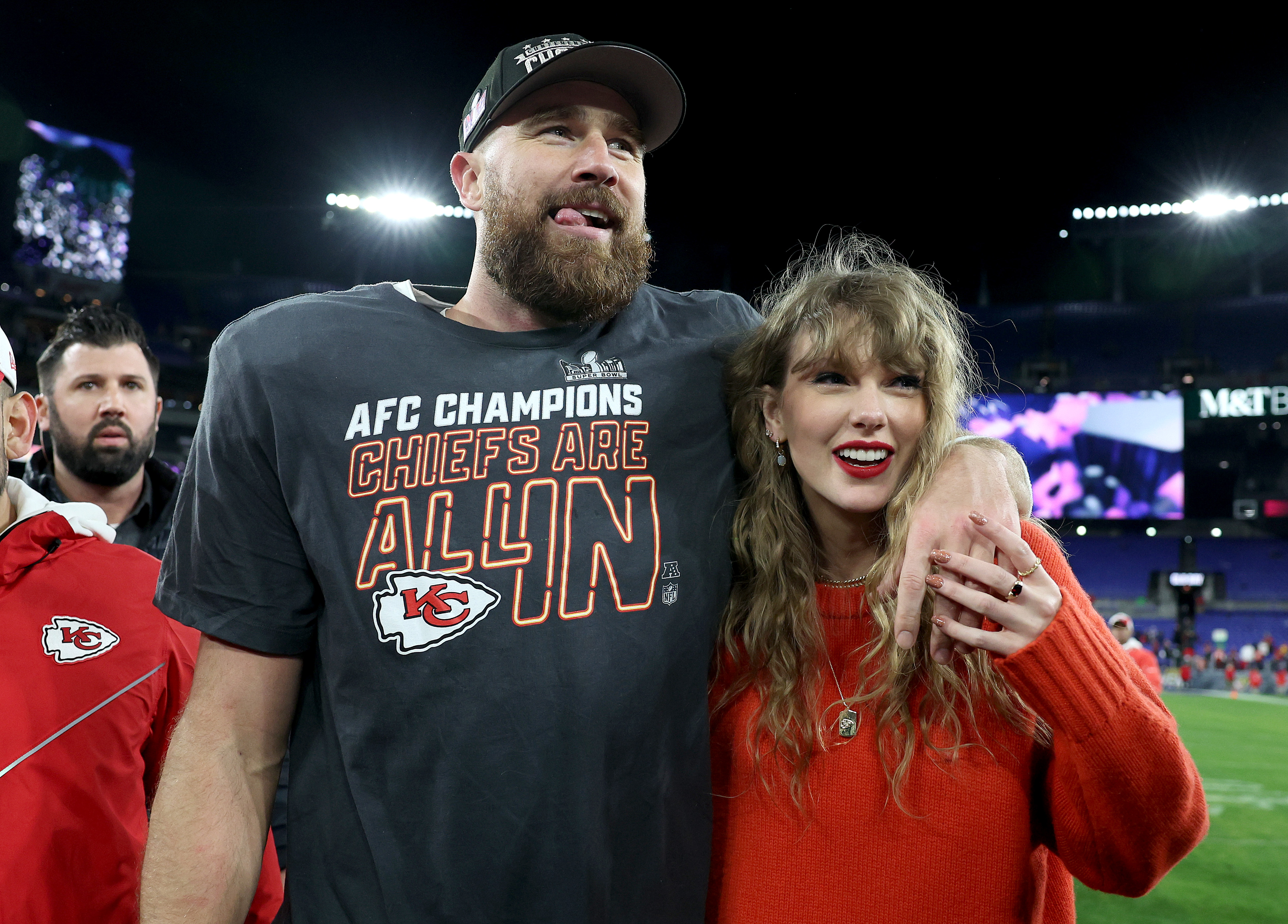Taylor Swift and Travis Kelce smile on the football field. 